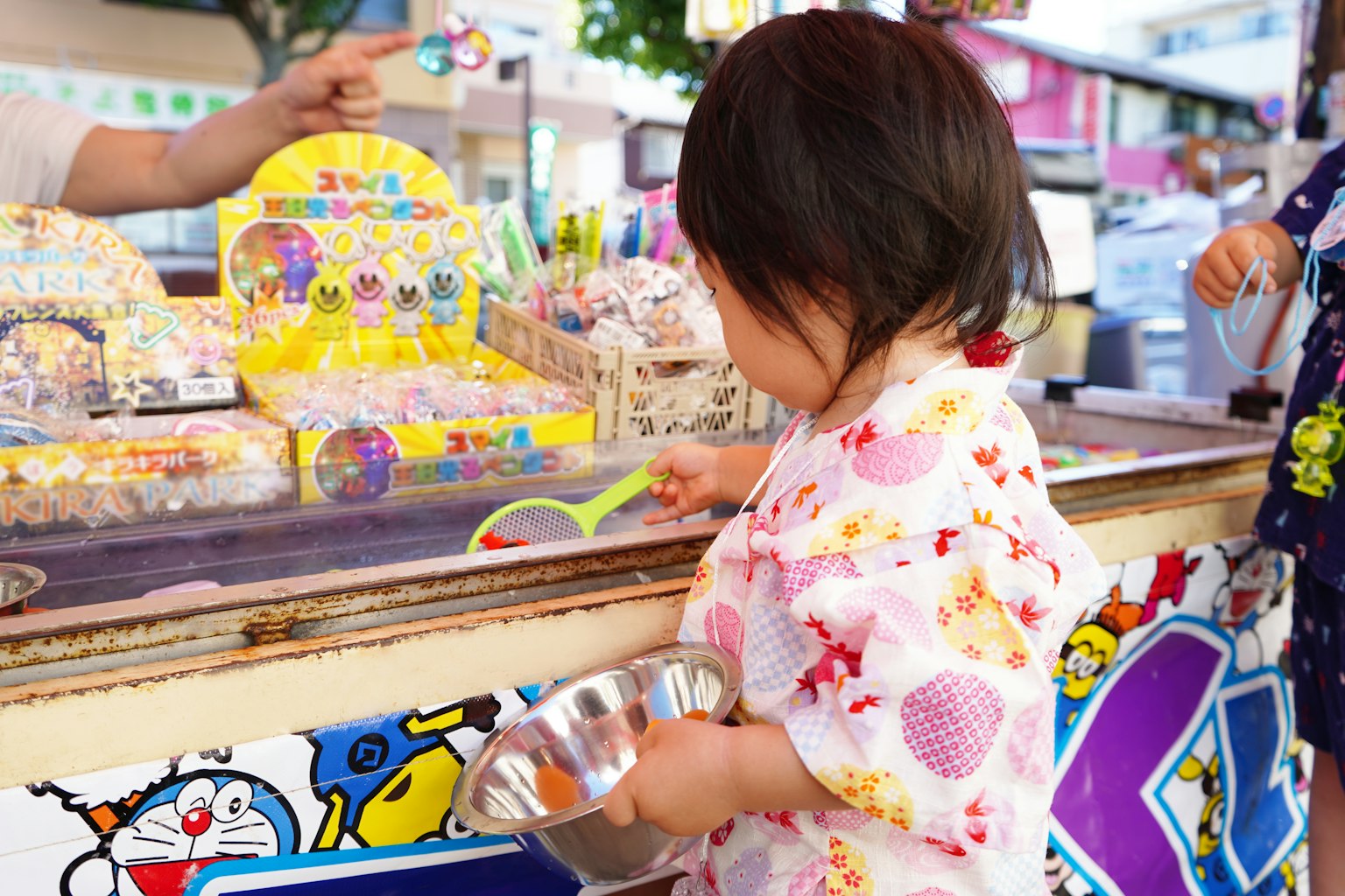 Una giovane ragazza in yukata floreale che si diverte a uno stand colorato in un festival