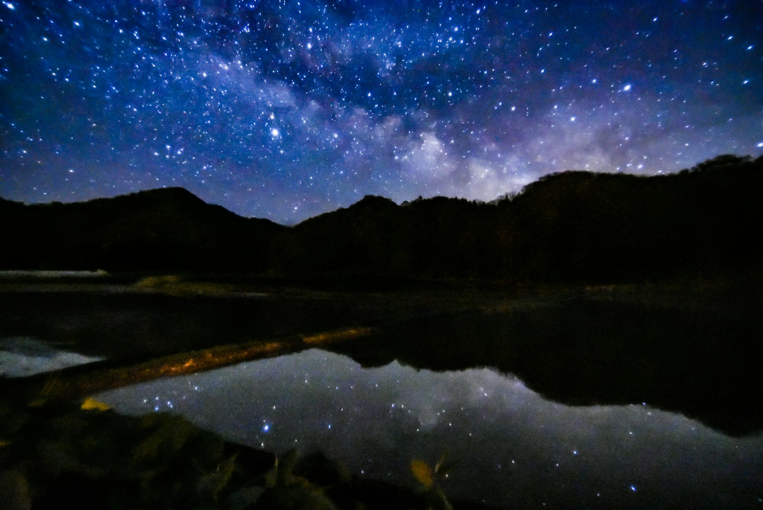 Cielo estrellado con siluetas de montañas reflejadas en un lago tranquilo