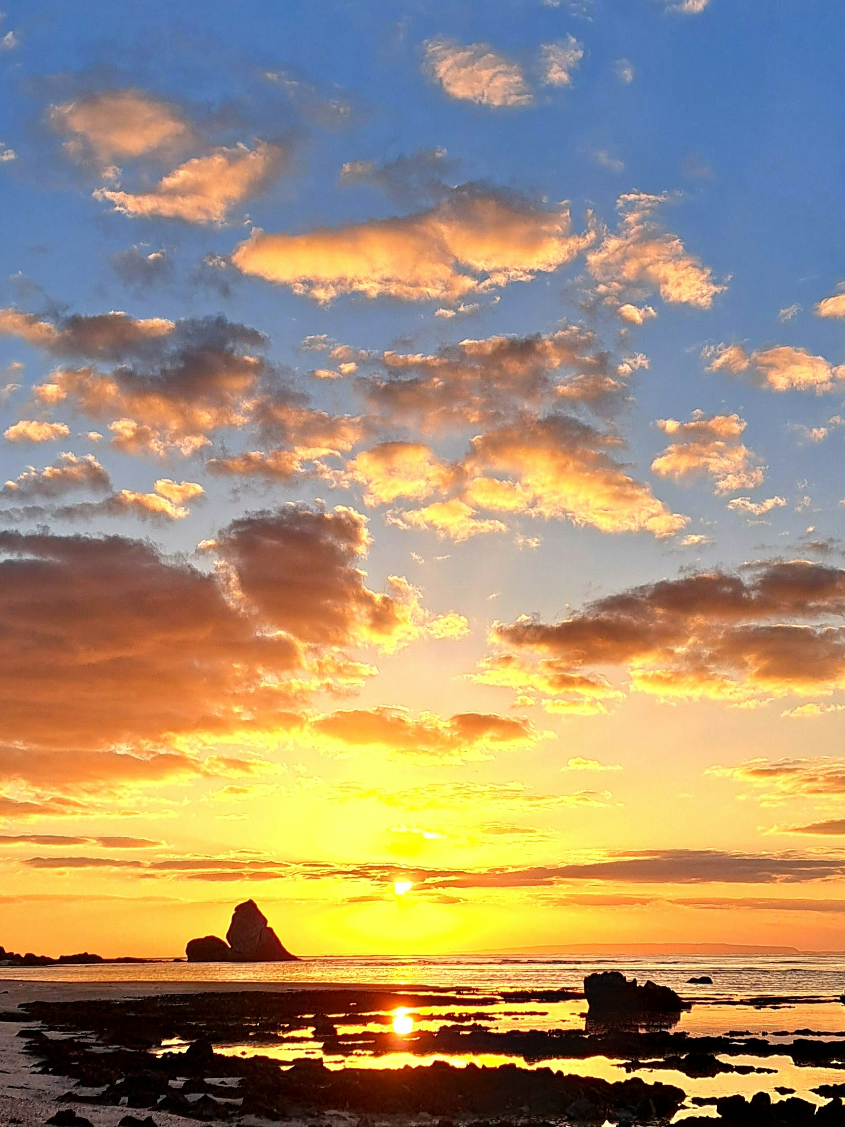 夕日に照らされる海岸の岩と水平線の雲