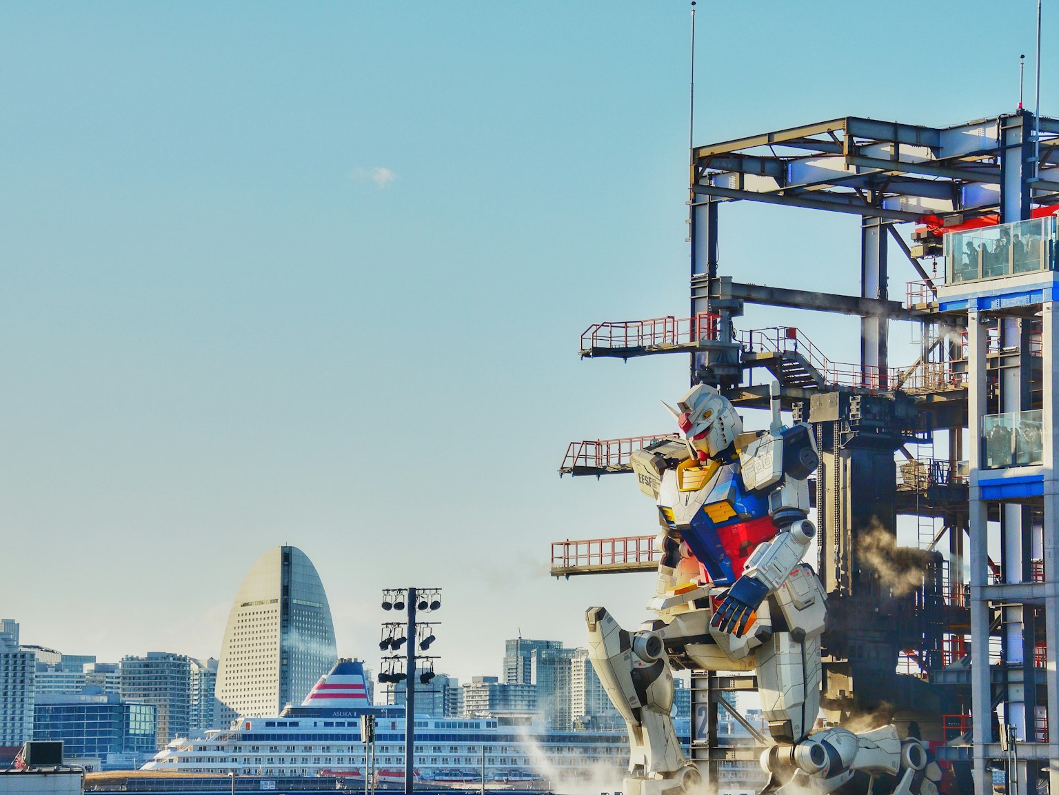 Giant Gundam statue in Yokohama with a cruise ship and skyscrapers under a blue sky