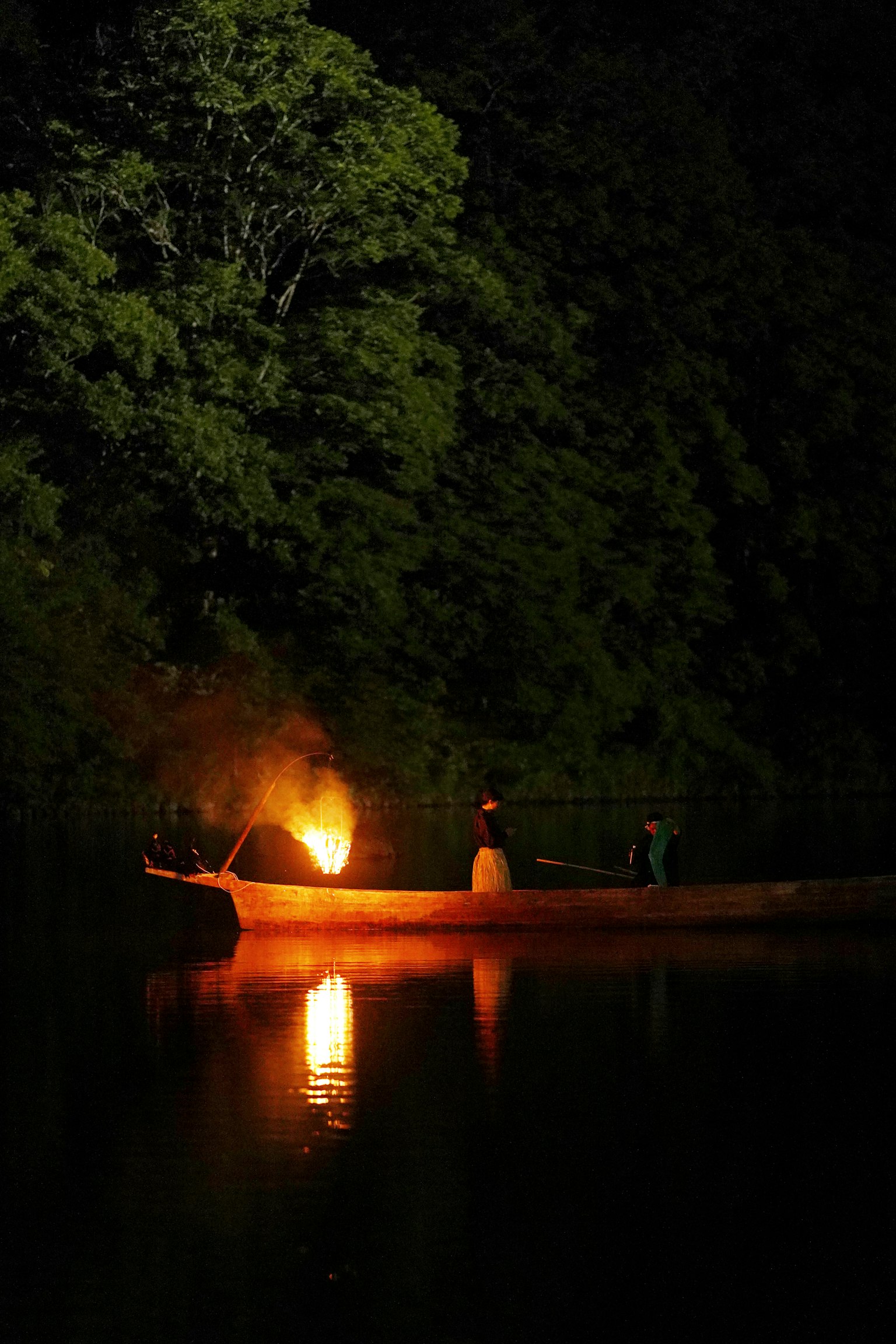 Orang-orang di perahu di malam hari dengan api yang memantul di air