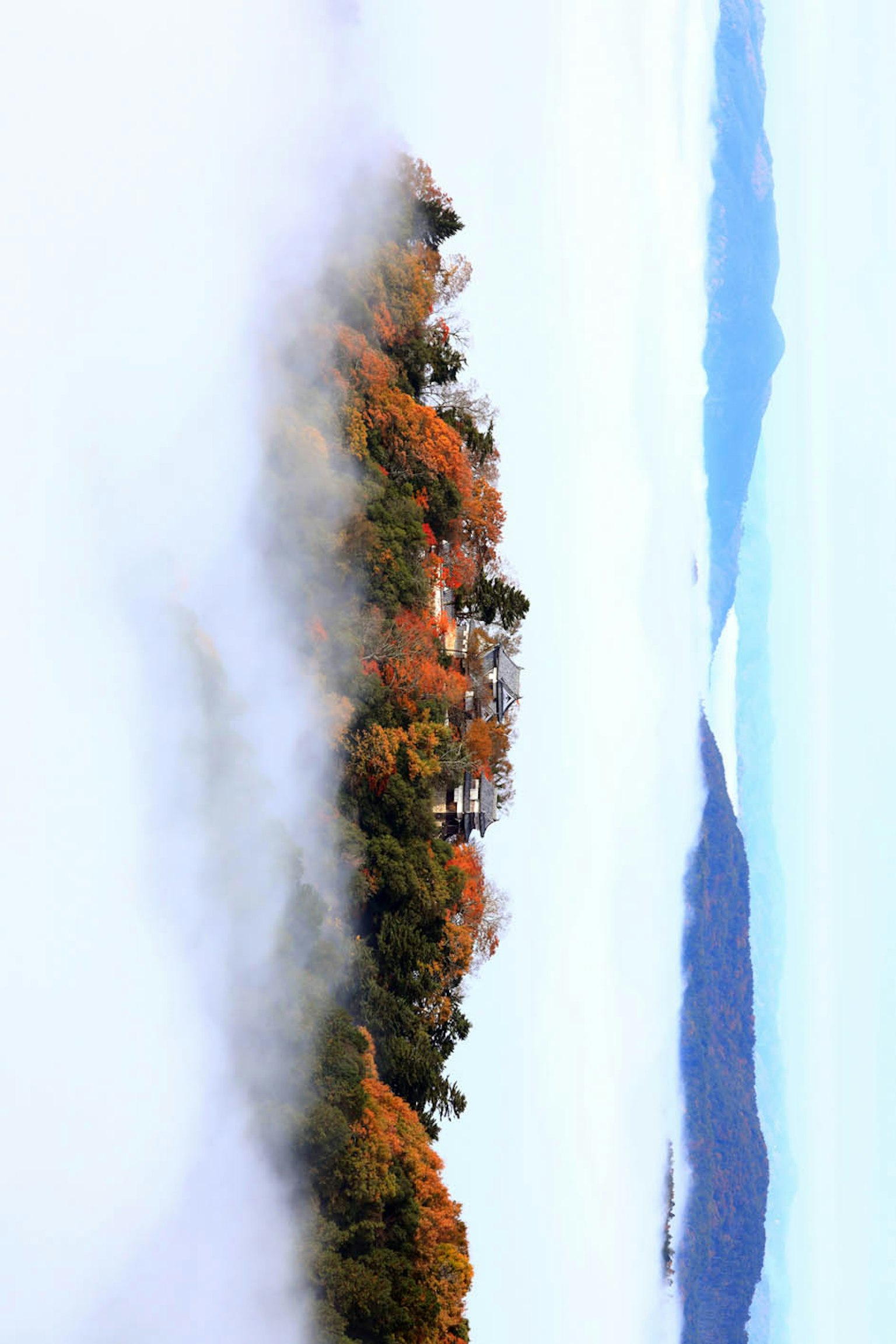 Herbstlandschaft in Nebel gehüllt mit grünen und orangefarbenen Bäumen auf den Bergen