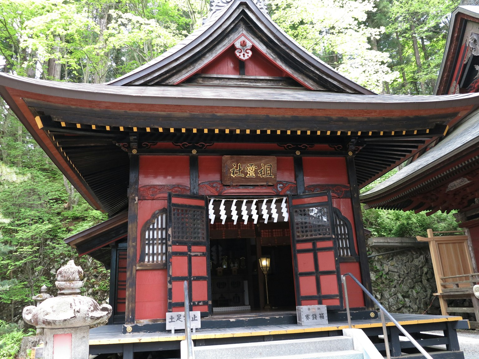 Exterior of a shrine with a red roof and wooden structure Traditional Japanese architectural style Surrounded by lush greenery