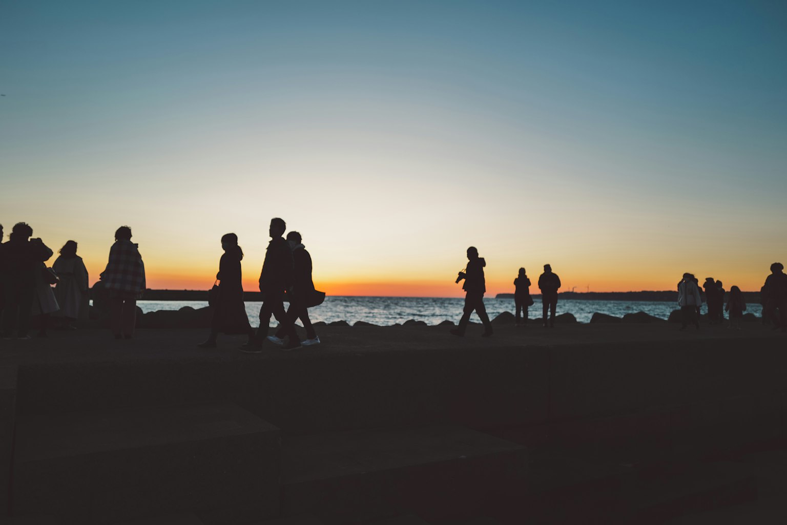 Silhouette di persone che camminano lungo la spiaggia al tramonto