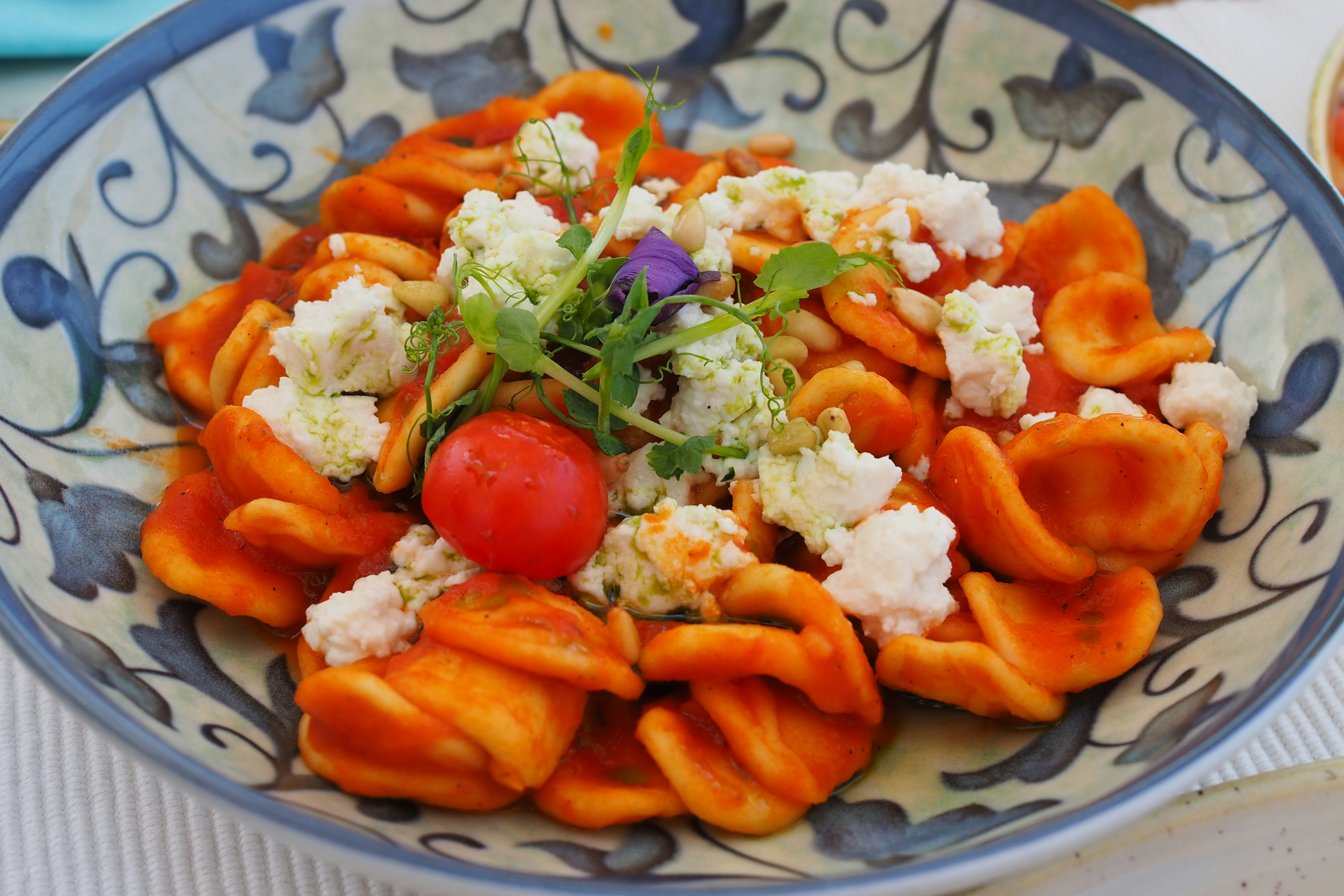 Orange pasta dish topped with tomato, cheese, and herbs