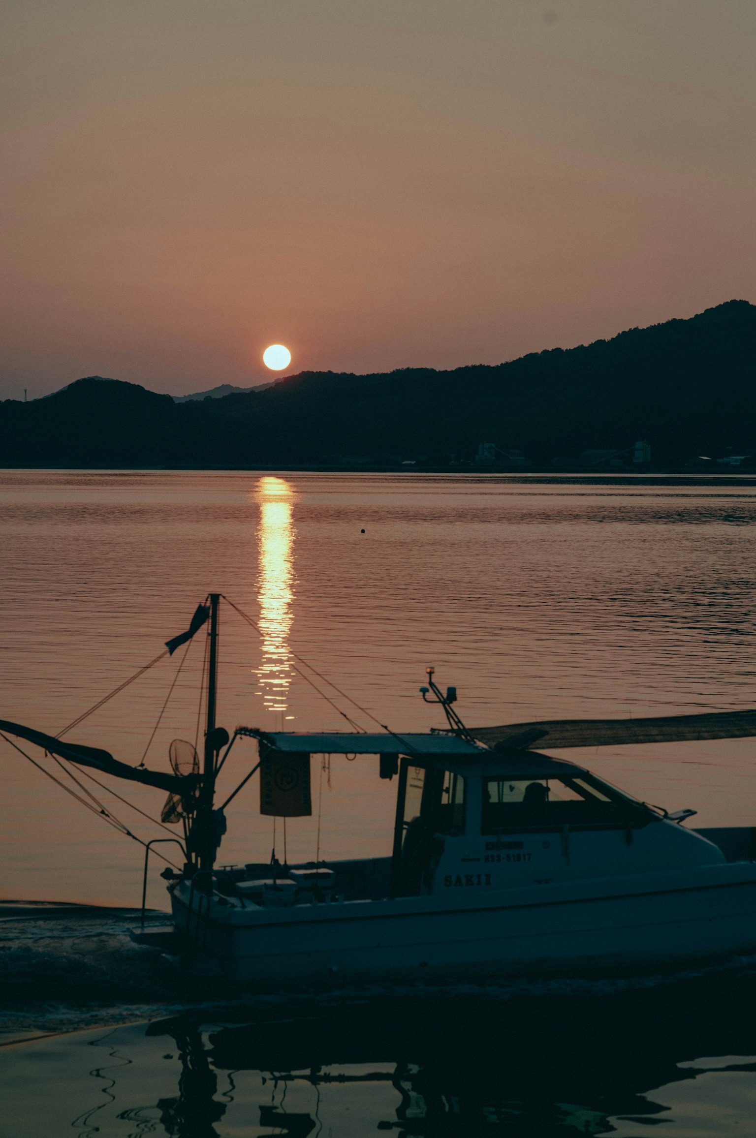 Silhouette eines Fischerbootes vor einem Sonnenuntergang, der sich im Wasser spiegelt