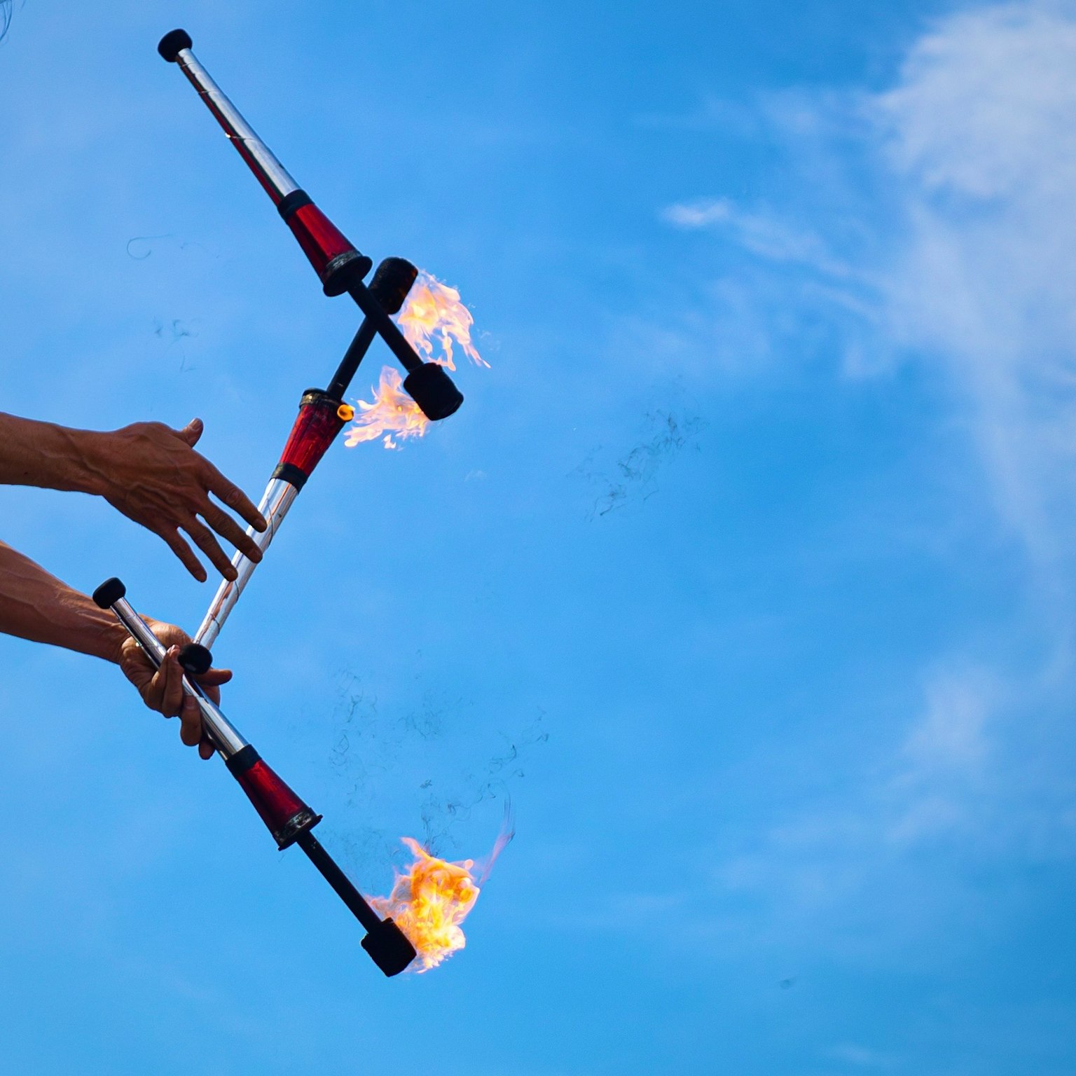 Mains tenant des torches de jonglage enflammées contre un ciel bleu