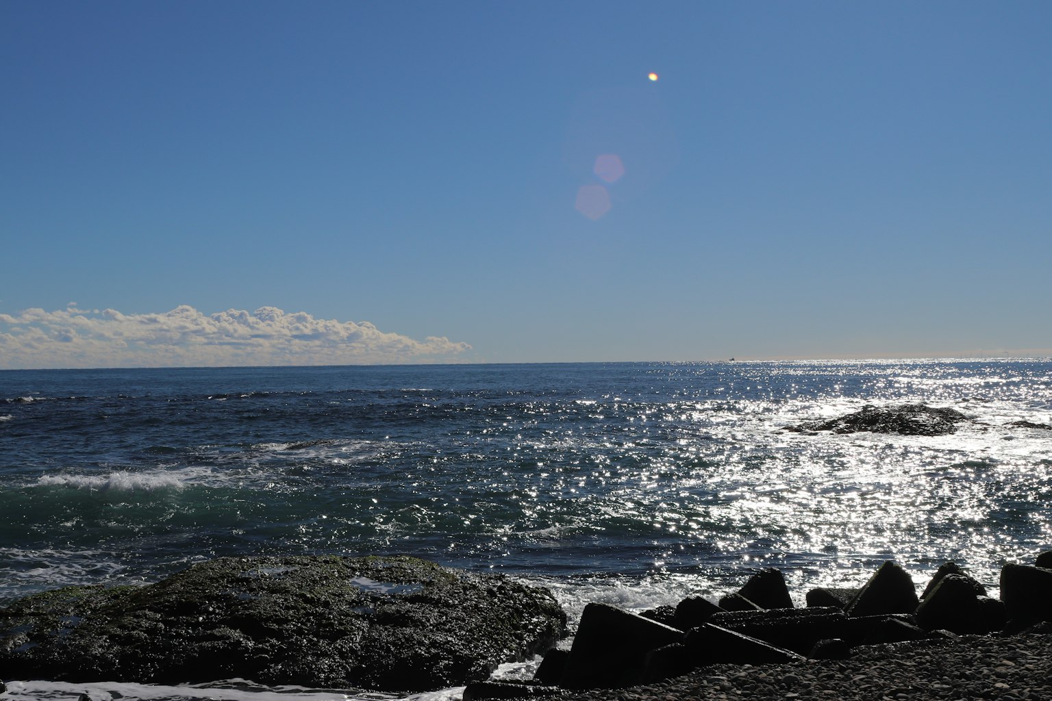 Vista escénica del cielo azul y el océano brillante con rocas y olas visibles
