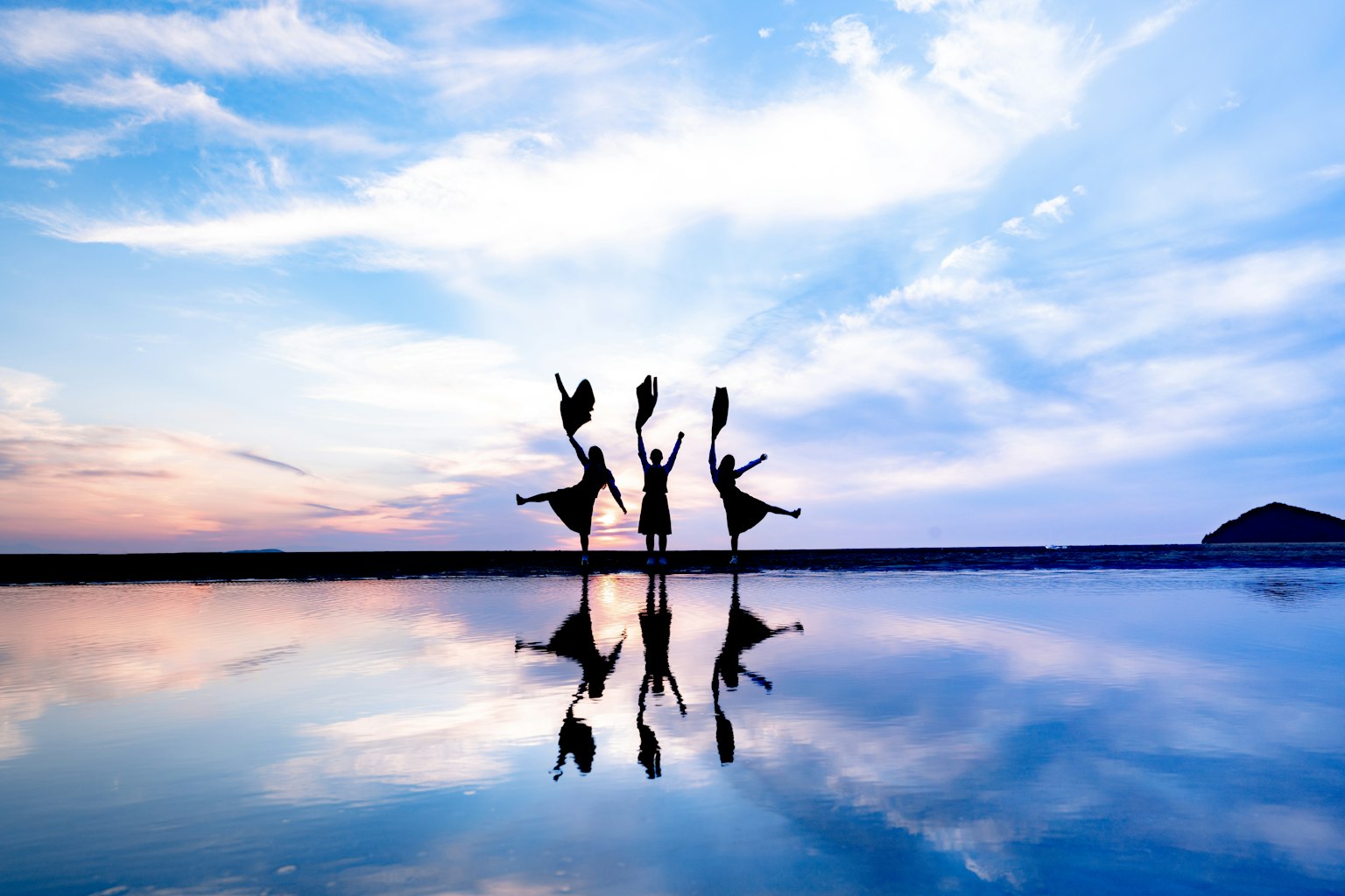 Silhouettes of people dancing reflected on water with a blue sky