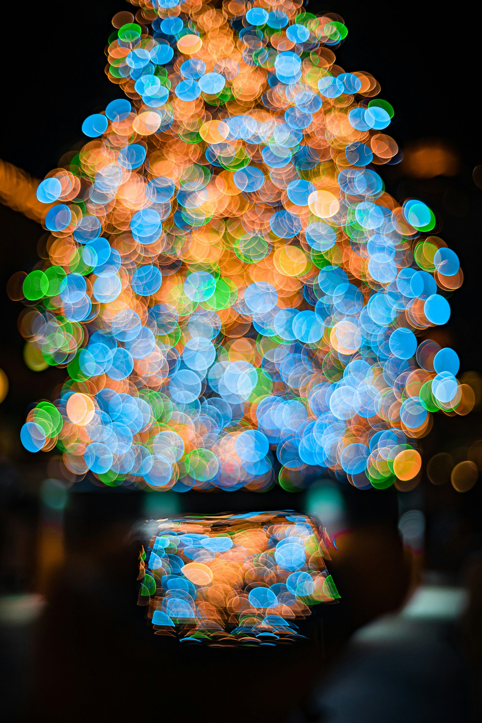 Una mano sosteniendo un teléfono inteligente frente a un árbol de Navidad borroso con luces coloridas
