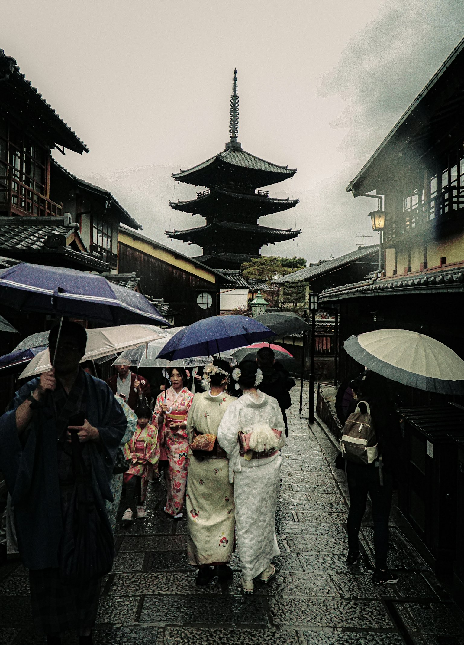 People in traditional kimonos walking under umbrellas in a historic street