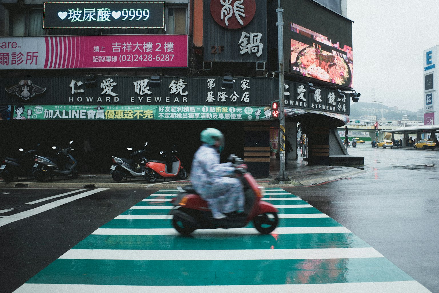Scooter rouge traversant une voie piétonne verte par un jour de pluie