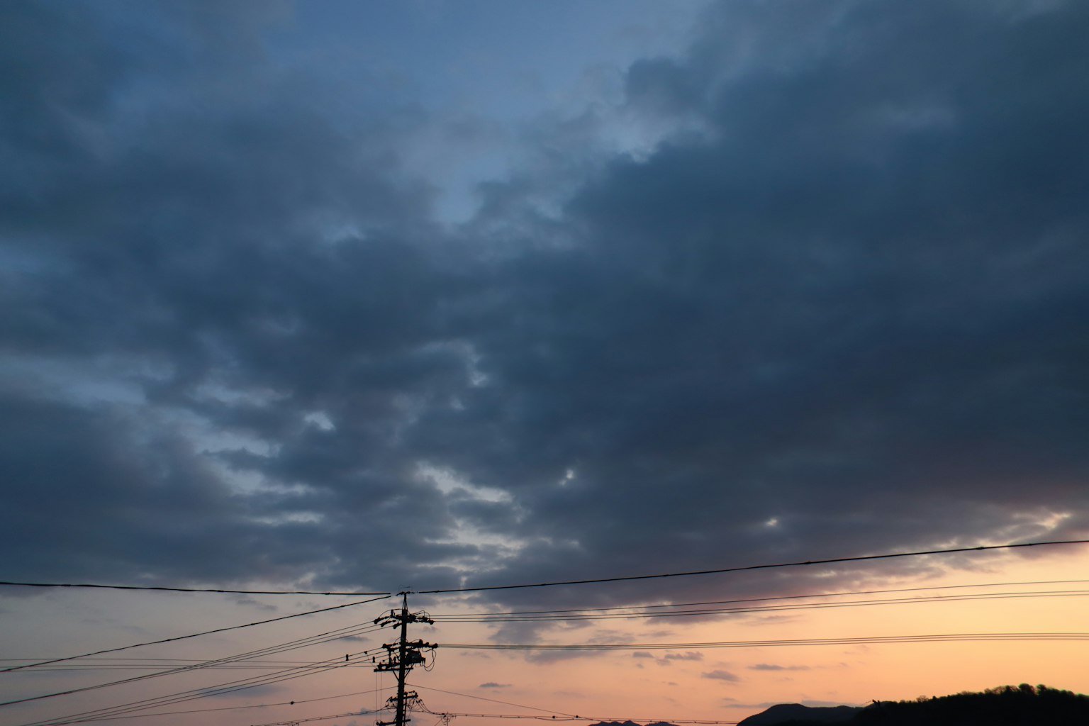 Un paysage avec des nuages sombres dans un ciel au coucher du soleil avec des lignes électriques et des collines visibles
