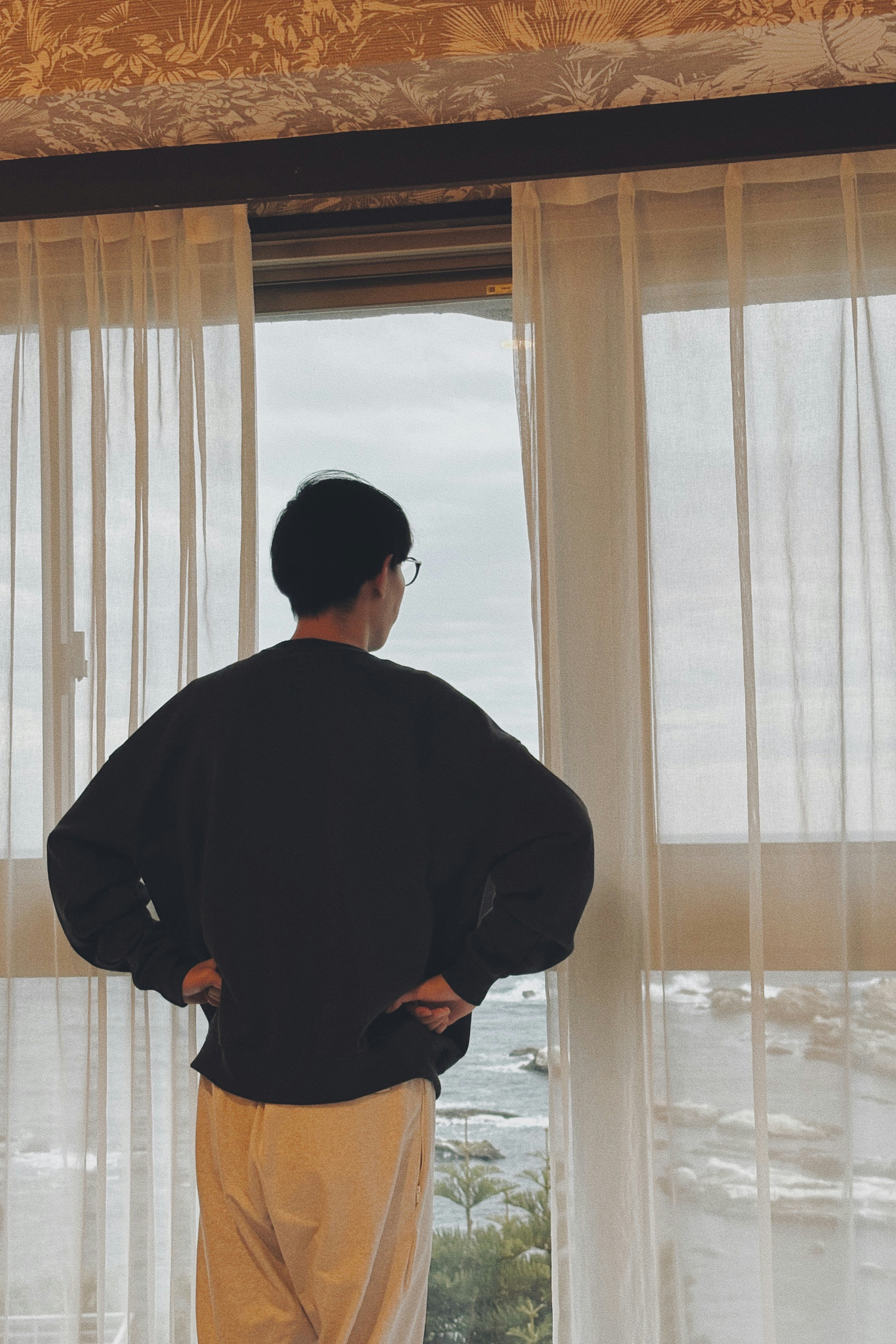 indoor scene with a person seen from behind near a window and curtains