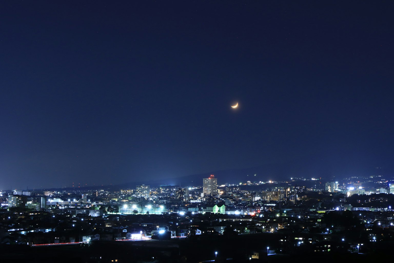 Pemandangan kota malam dengan bangunan yang diterangi dan bulan sabit