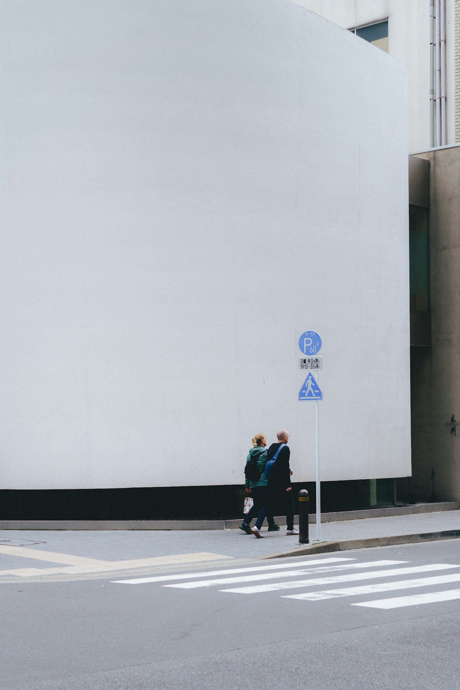 Due pedoni che attraversano un incrocio con un muro di edificio bianco sullo sfondo