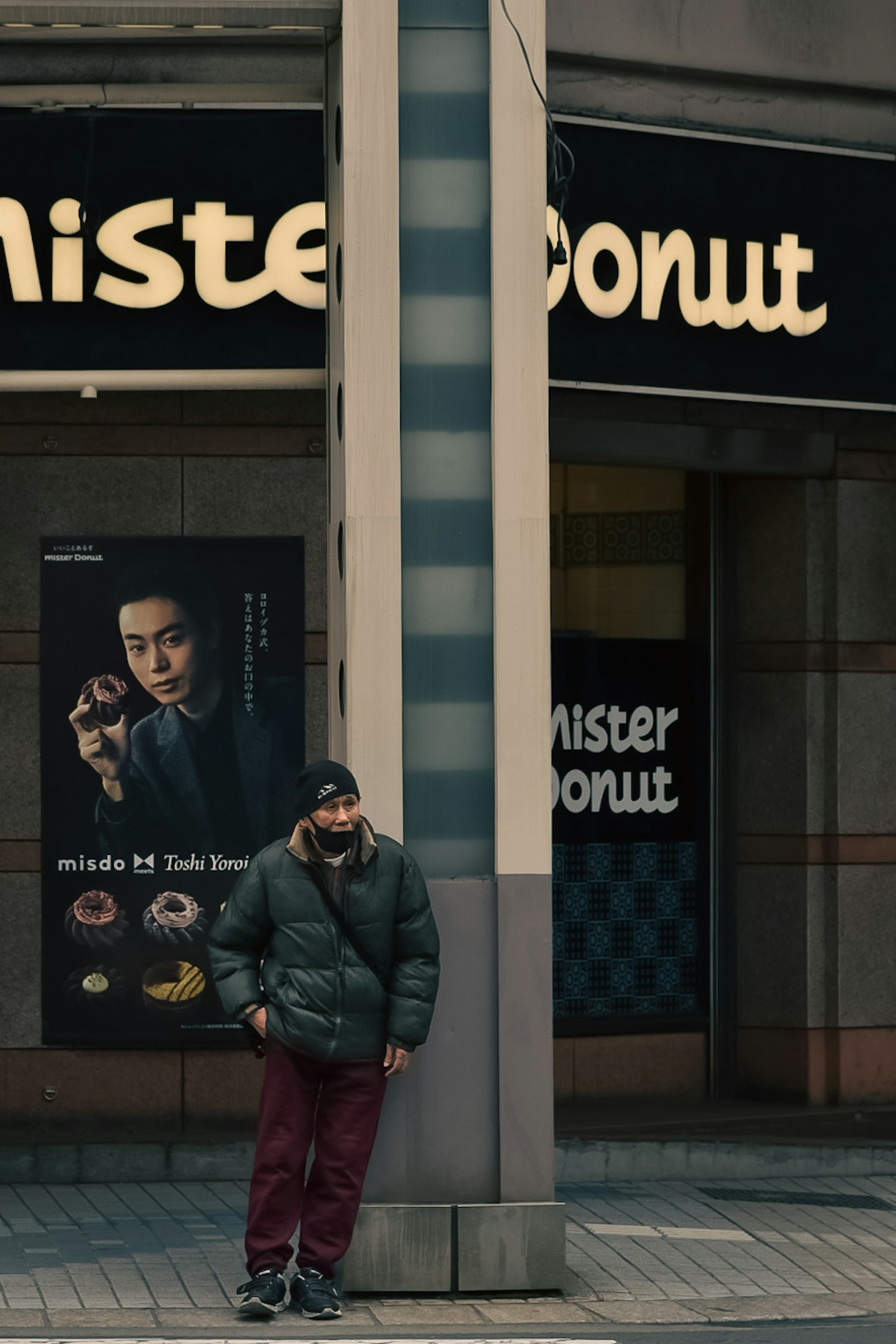 Uomo in piedi all'angolo della strada vicino al cartello Mister Donut