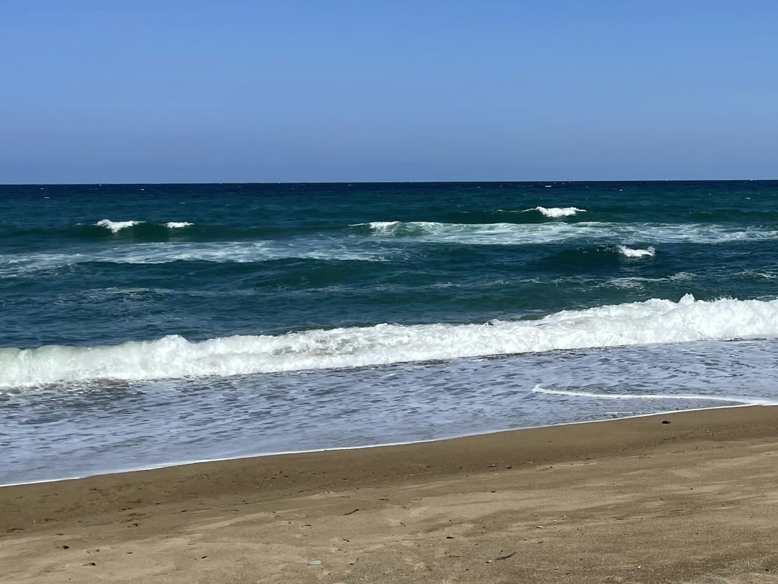 Eine malerische Aussicht auf einen blauen Ozean mit sanften weißen Wellen, die an einen Sandstrand schlagen