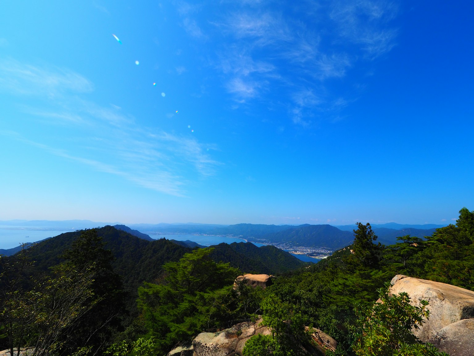 ทิวทัศน์ที่สวยงามพร้อมท้องฟ้าสีฟ้าและภูเขาที่มีต้นไม้เขียวขจีและหิน