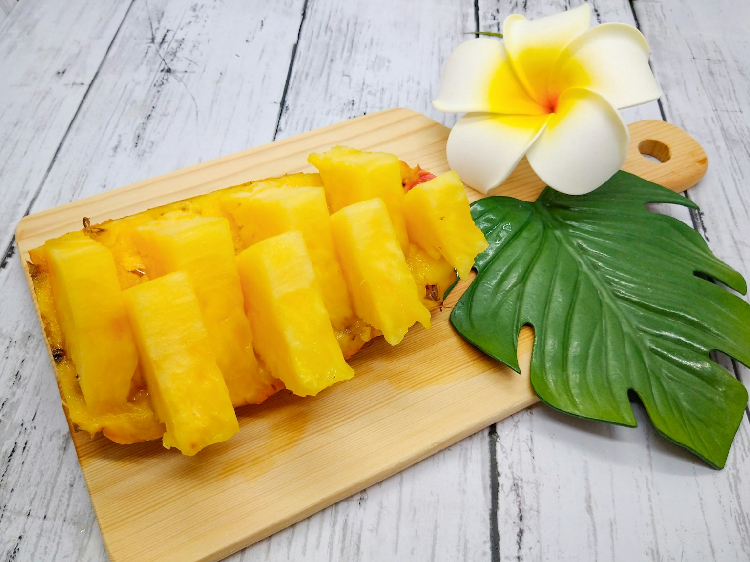 Geschnittene Ananas auf einem Holzbrett mit einer dekorativen Blume