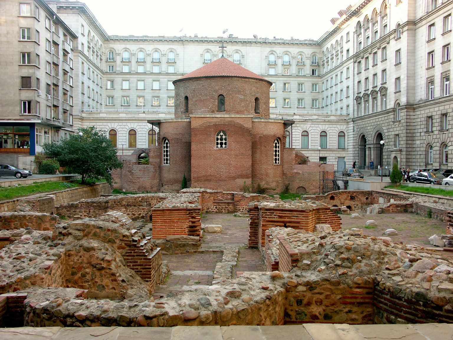 Ancient ruins with a round brick structure surrounded by modern buildings