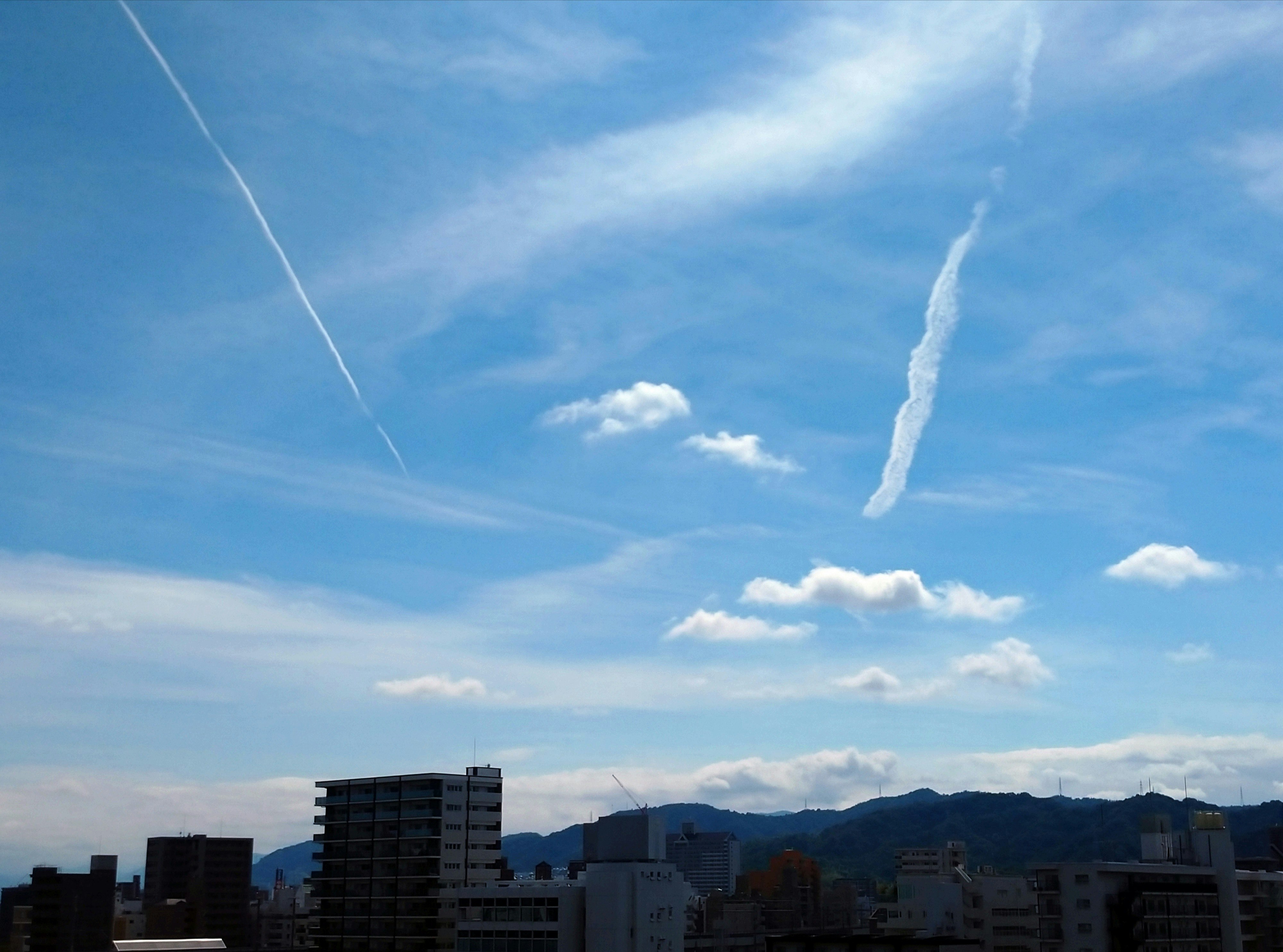 雲の広がる青空と細い飛行機雲のある街並み