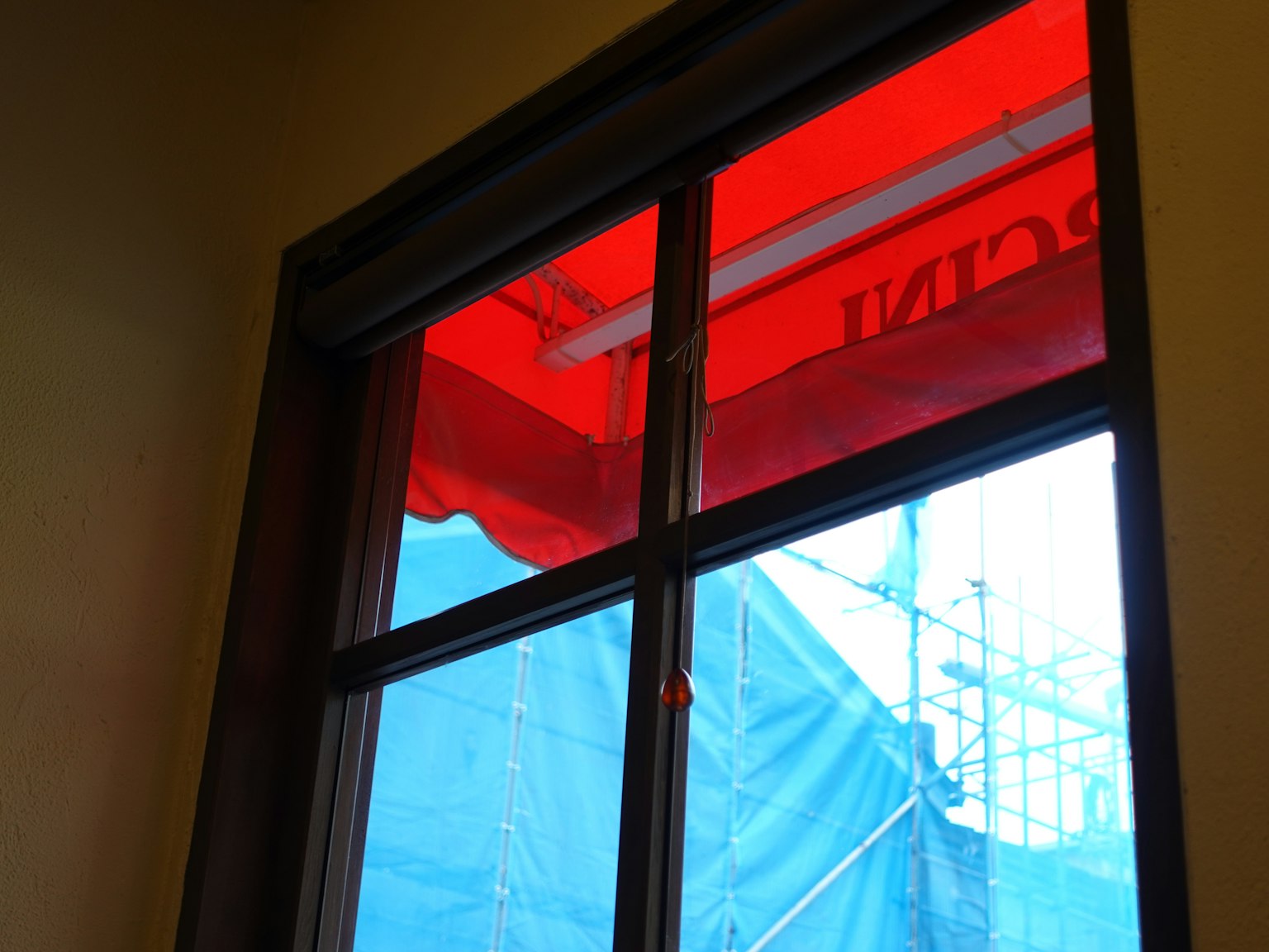Pemandangan interior jendela dengan kanopi merah dan terpal biru di luar