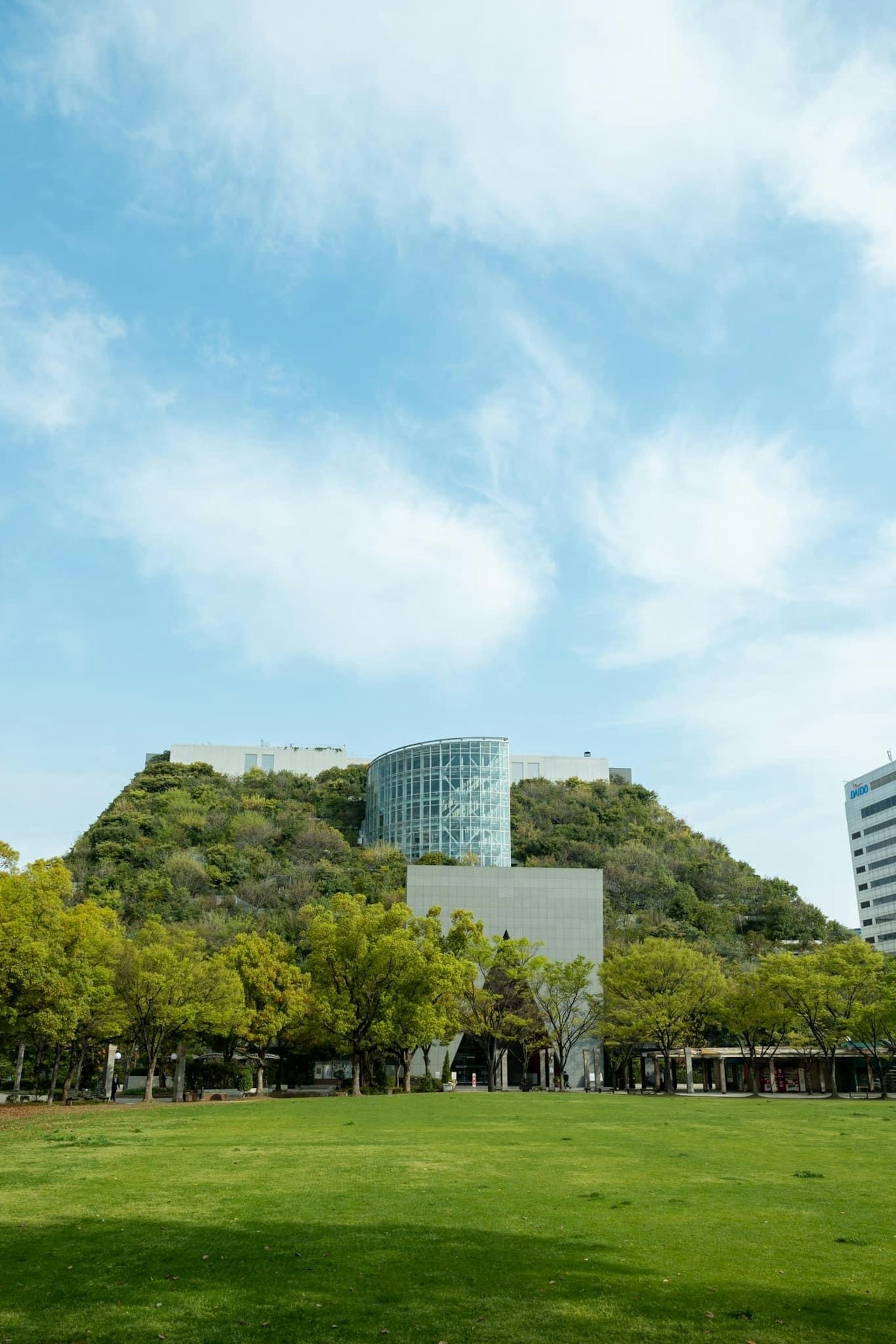 A landscape featuring a modern building on a lush green hill