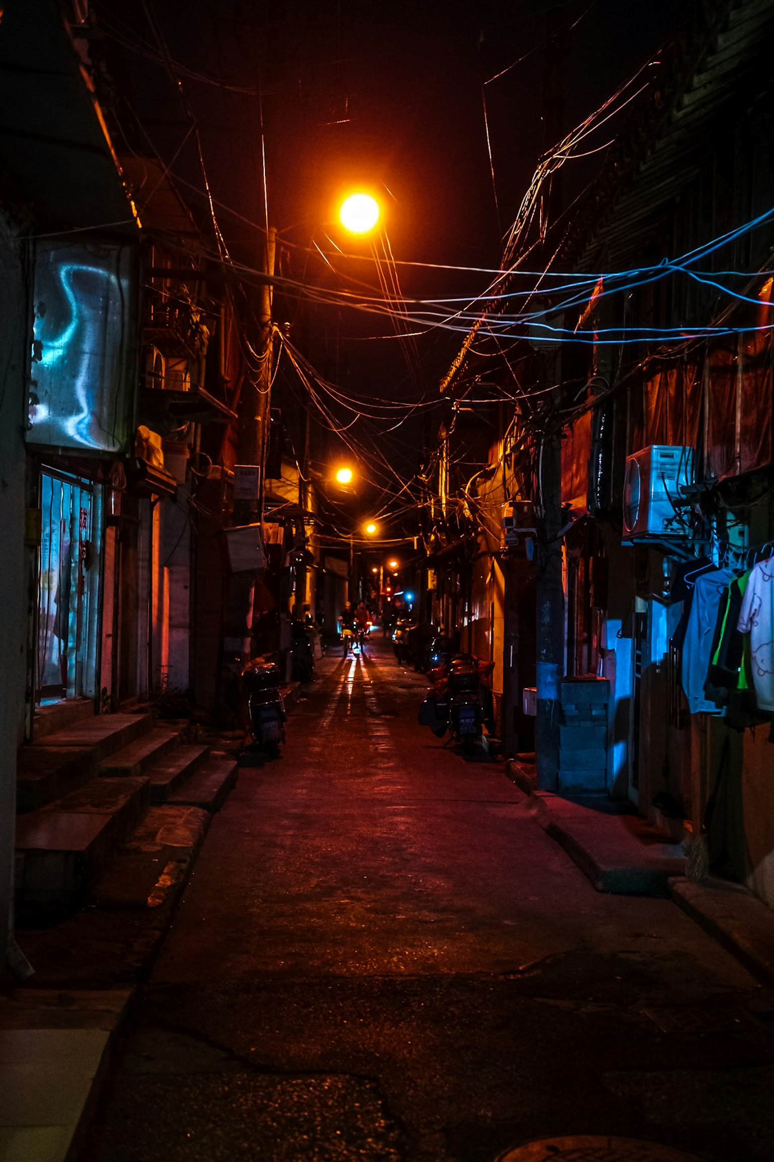 Schmale Gasse bei Nacht beleuchtet von Straßenlaternen und Neonlichtern