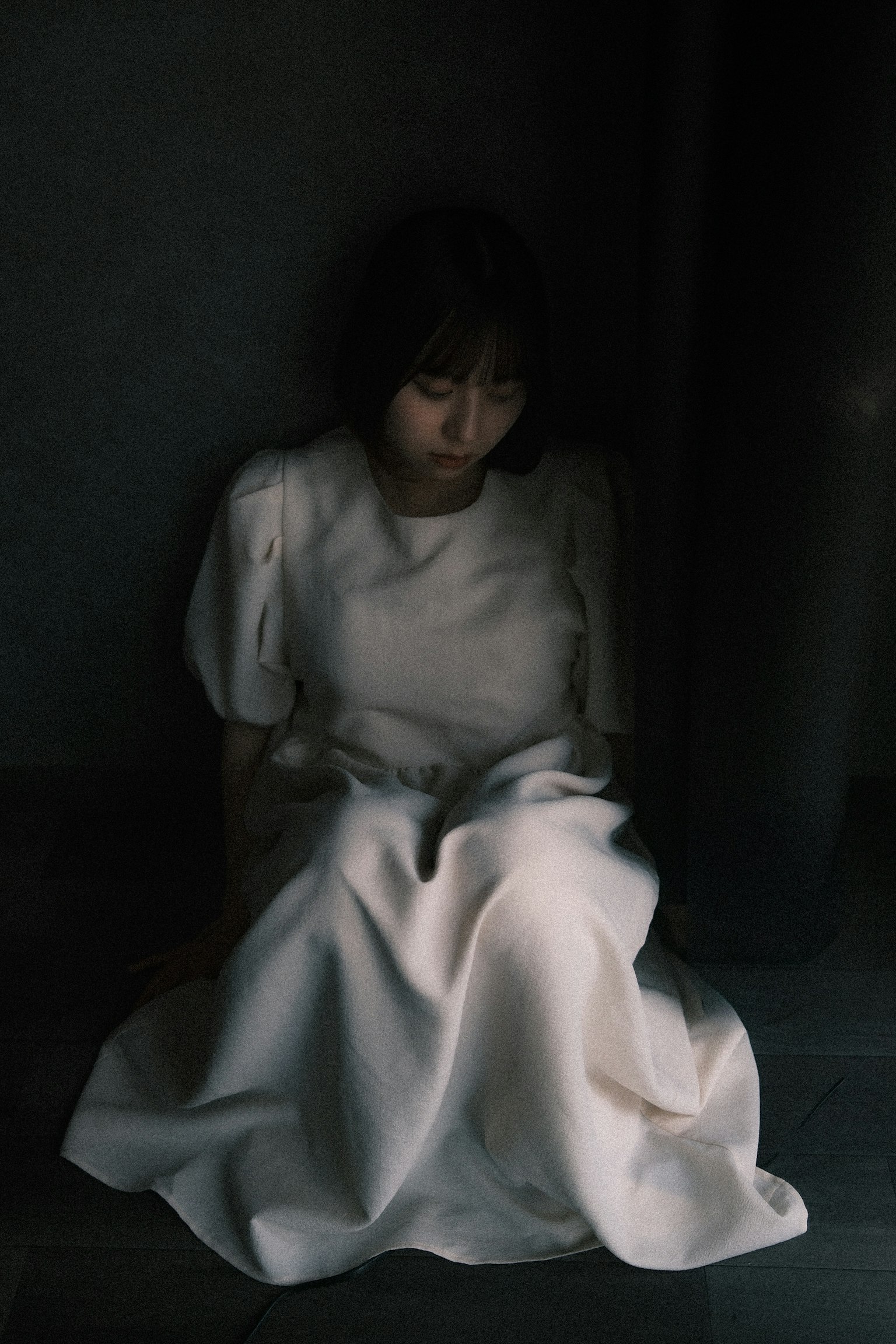 薄暗い部屋で白いドレスを着た女性が座っている
