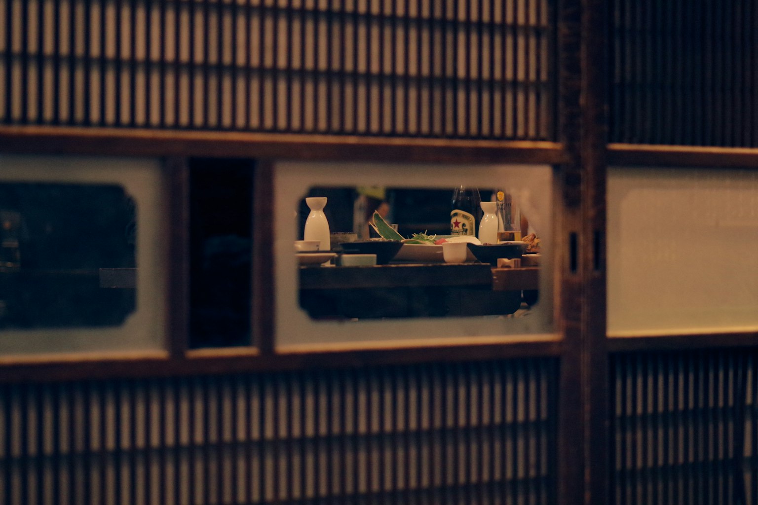 Vue à travers un shoji montrant de la vaisselle et des figurines dans une pièce japonaise traditionnelle