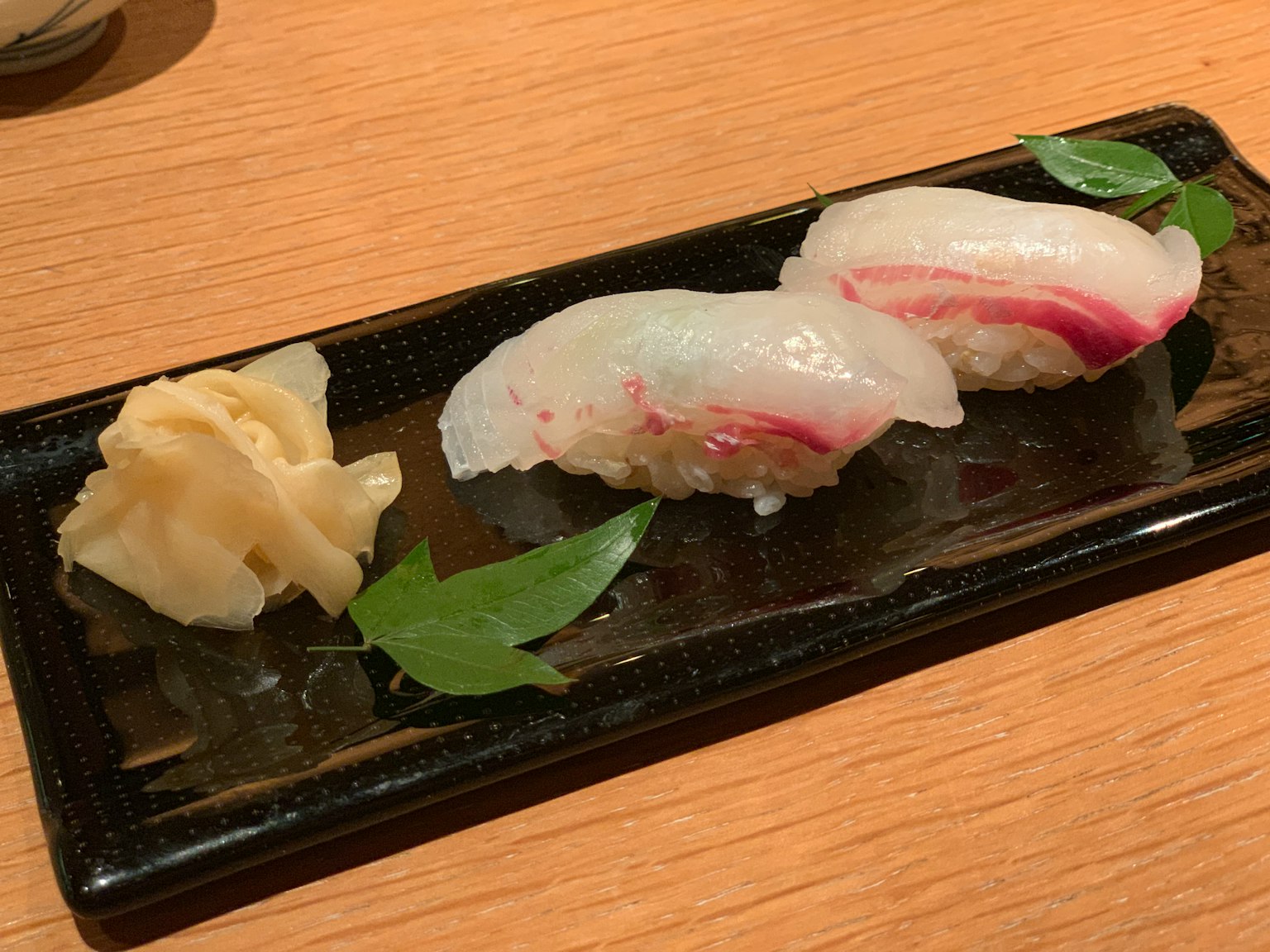 Sushi served on a black plate with pickled ginger on the side