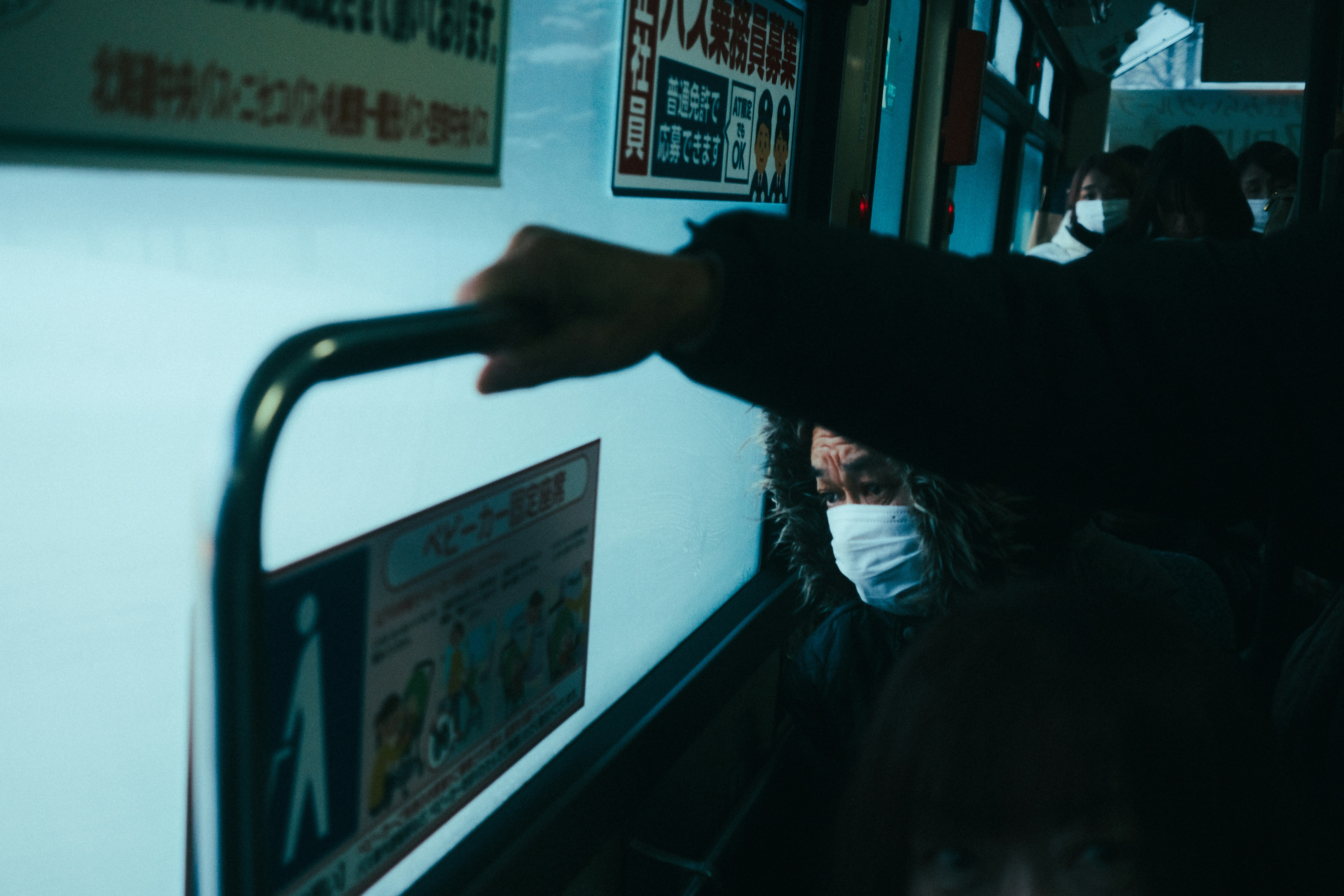 Personas con mascarilla en una parada de autobús de noche con vehículos pasando