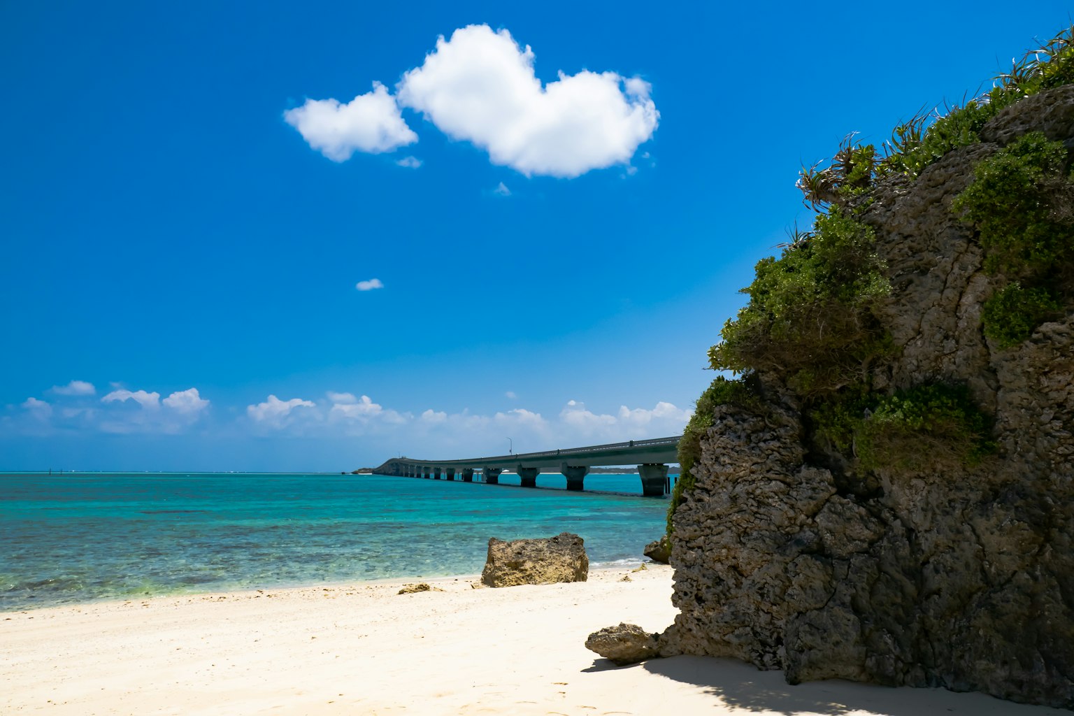 Panoramablick auf den blauen Ozean und den weißen Sandstrand mit einer Brücke in der Ferne