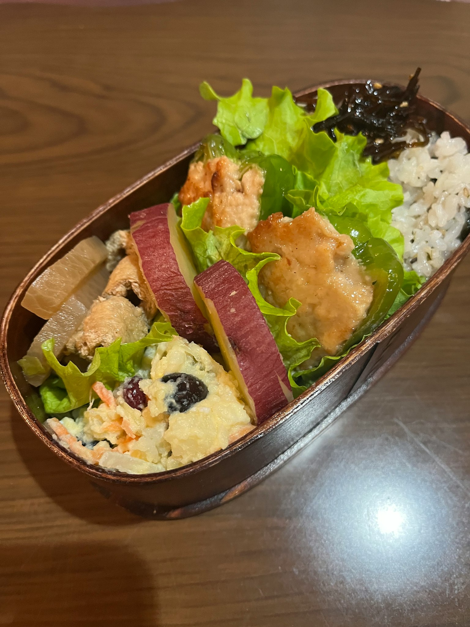 A bento box featuring green lettuce sweet potato rice nori and rolled omelet