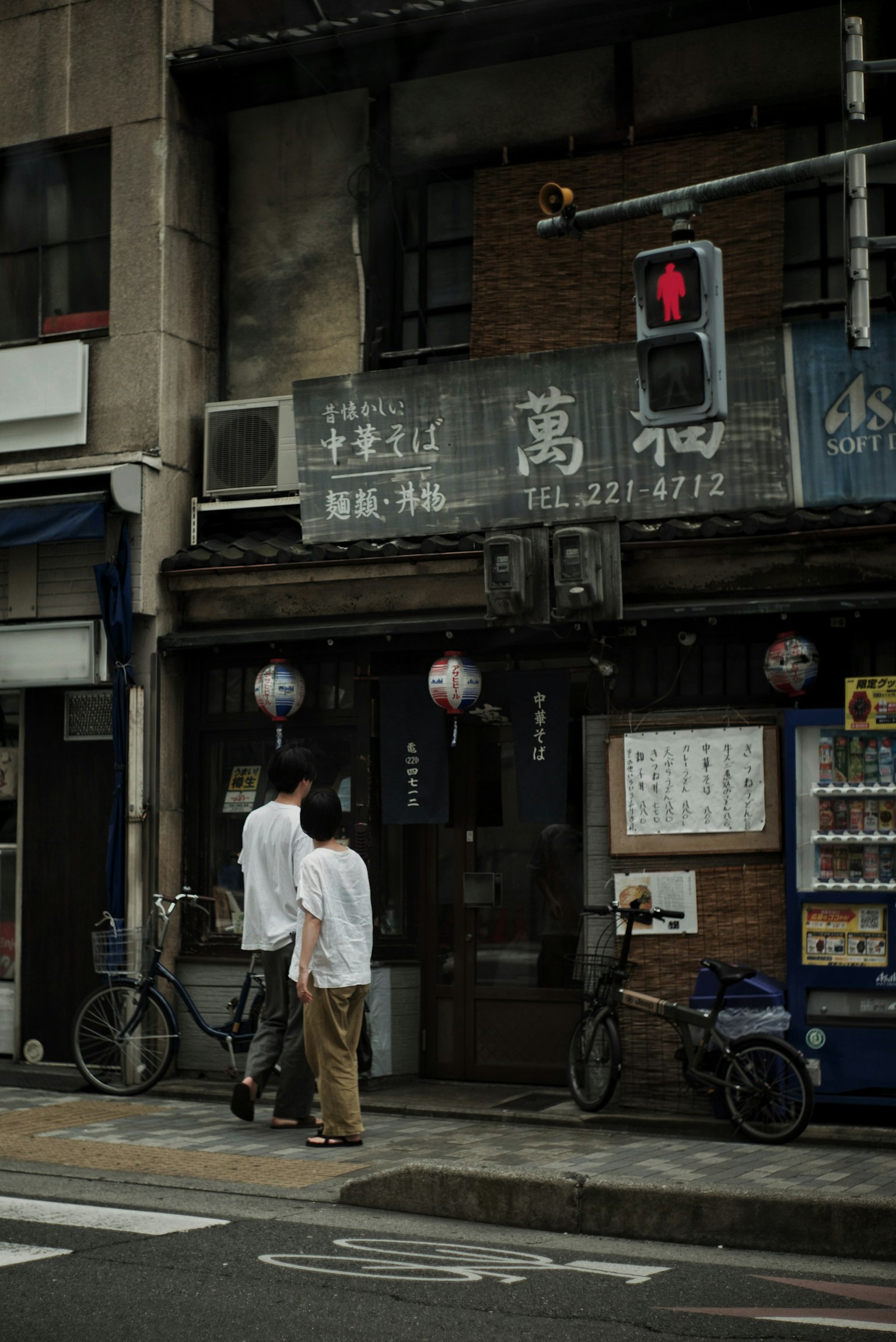 Zwei Personen gehen vor einem alten japanischen Restaurant auf einer Straße