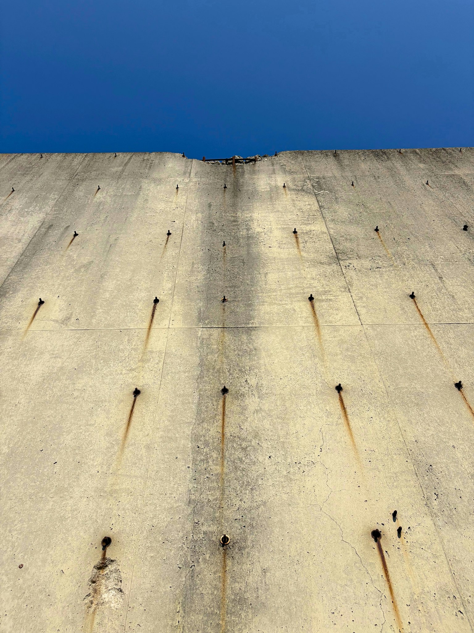 Close-up of a concrete wall under a blue sky featuring visible metal bolts