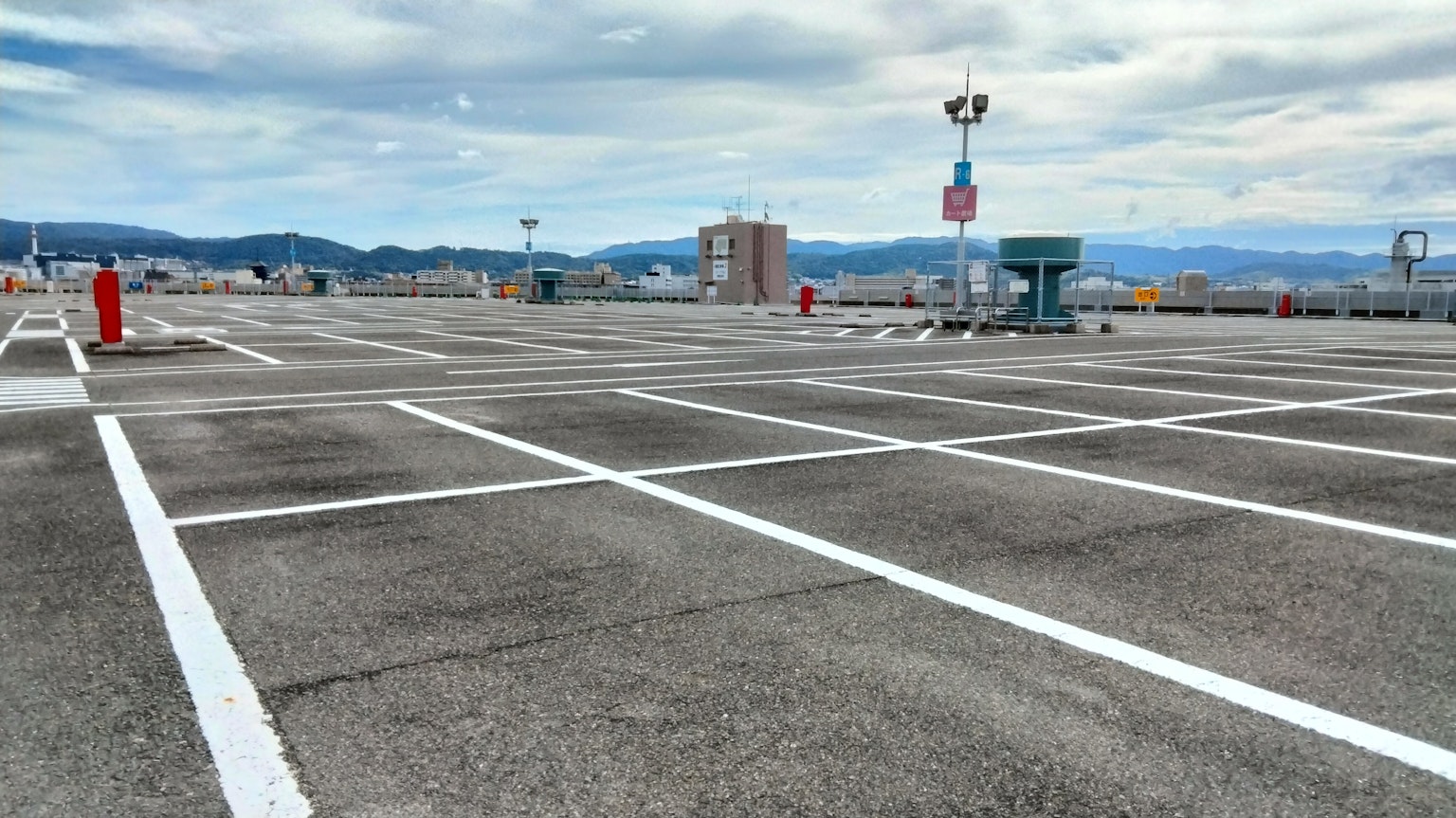 Estacionamiento vacío con amplios espacios Líneas blancas marcadas en el asfalto Cielo azul y montañas al fondo