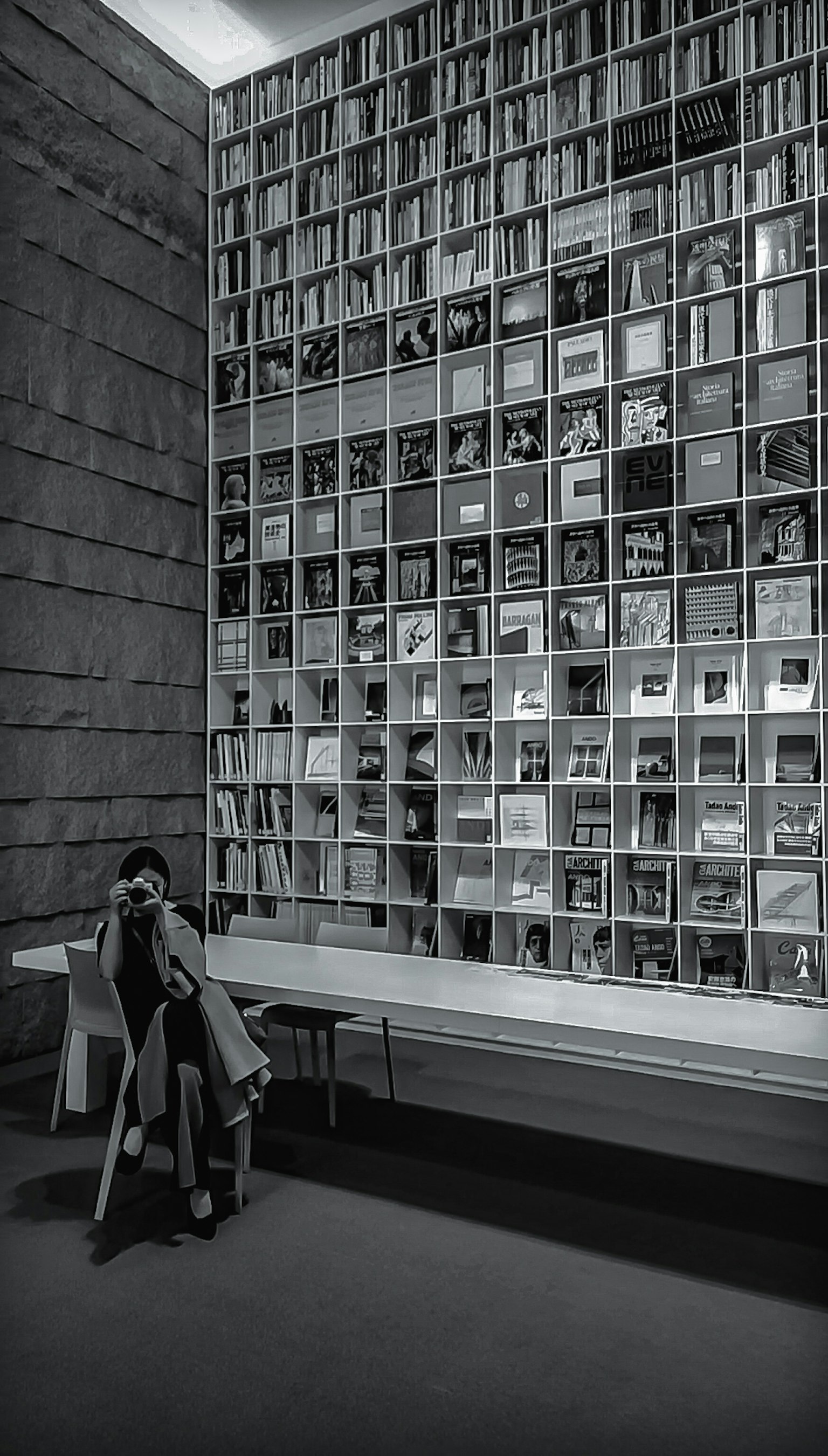 Un'immagine in bianco e nero di una donna seduta in una biblioteca con una parete di libri