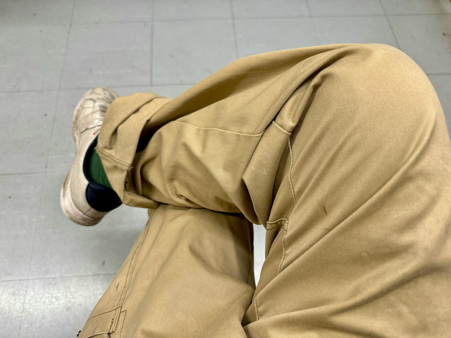Foto di gambe incrociate in pantaloni beige e scarpe bianche