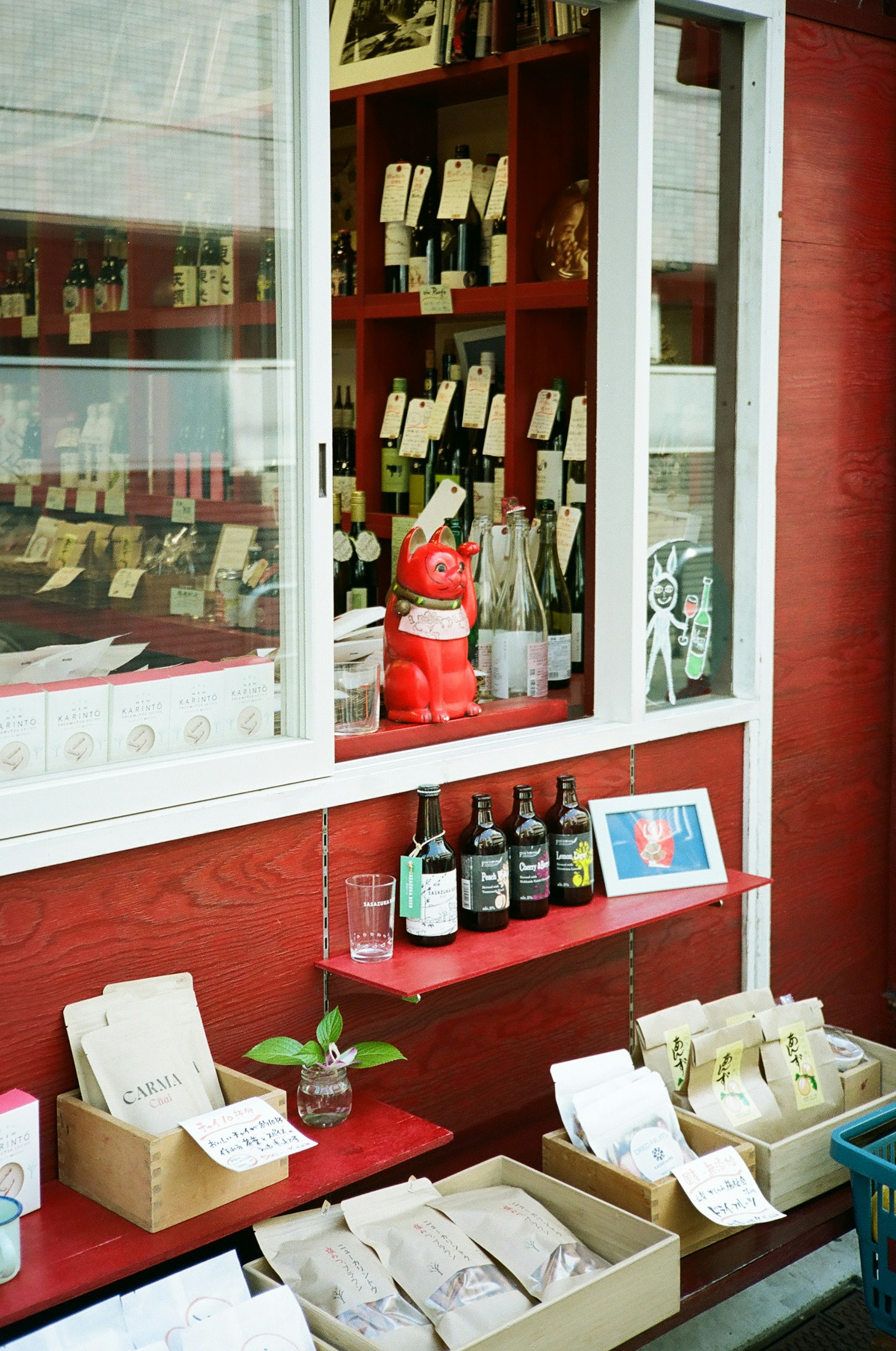หน้าต่างร้านเล็ก ๆ ที่มีผนังสีแดงแสดงผลิตภัณฑ์ต่าง ๆ และรูปปั้นแมวโชคดี