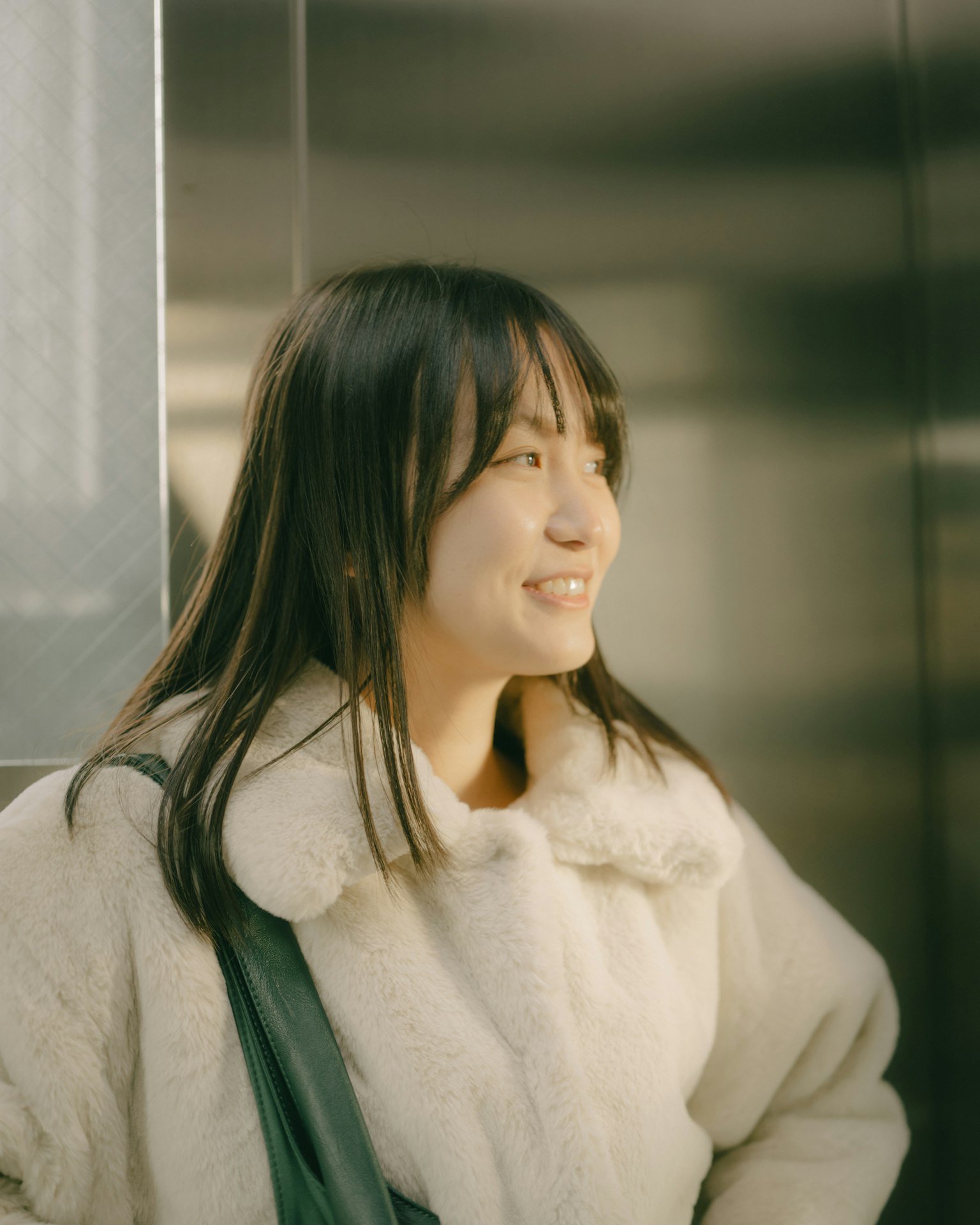 Una donna sorridente in un ascensore con un cappotto bianco
