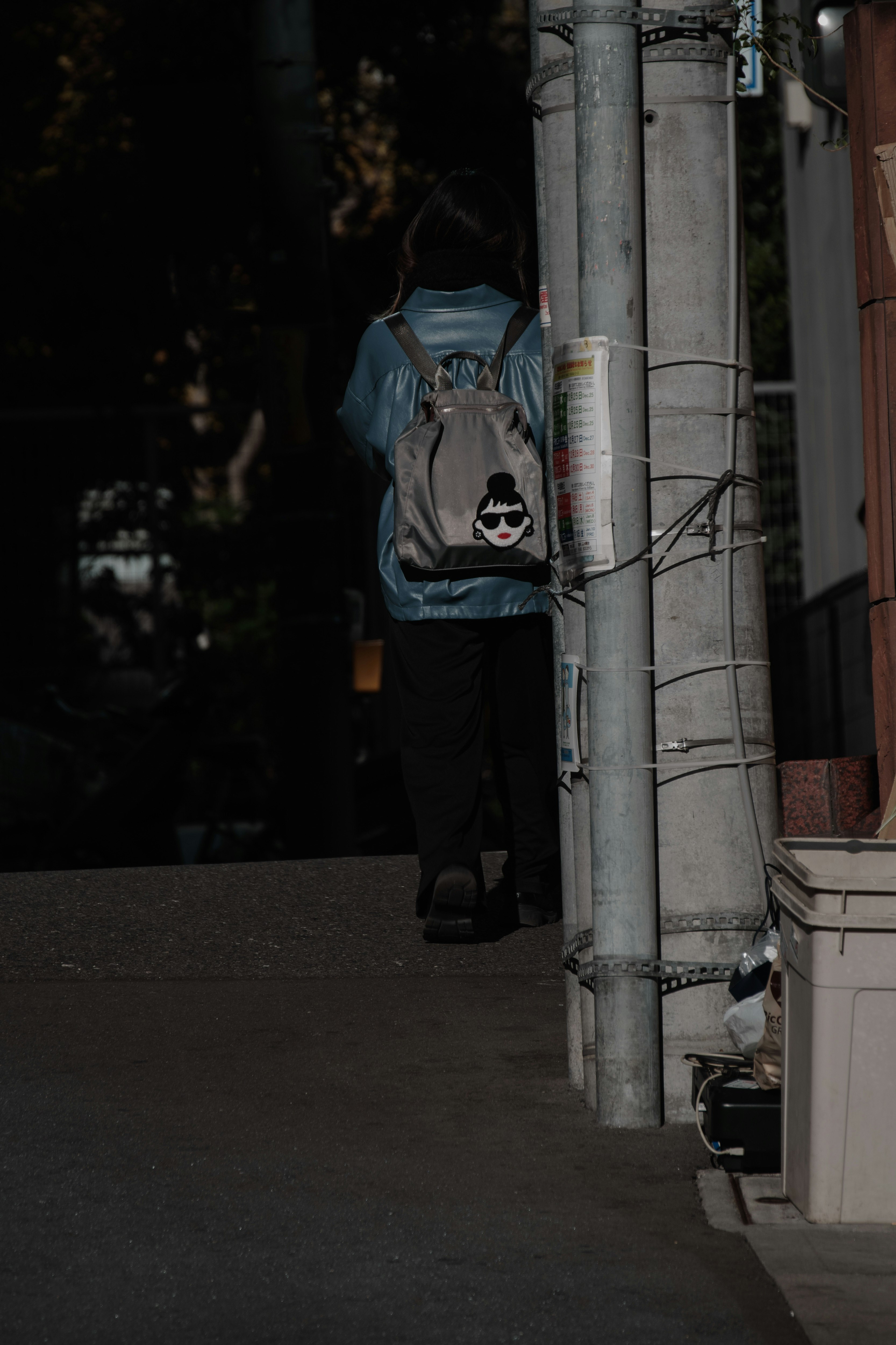 東京の路地でサングラスとバックパックの人物が立つ