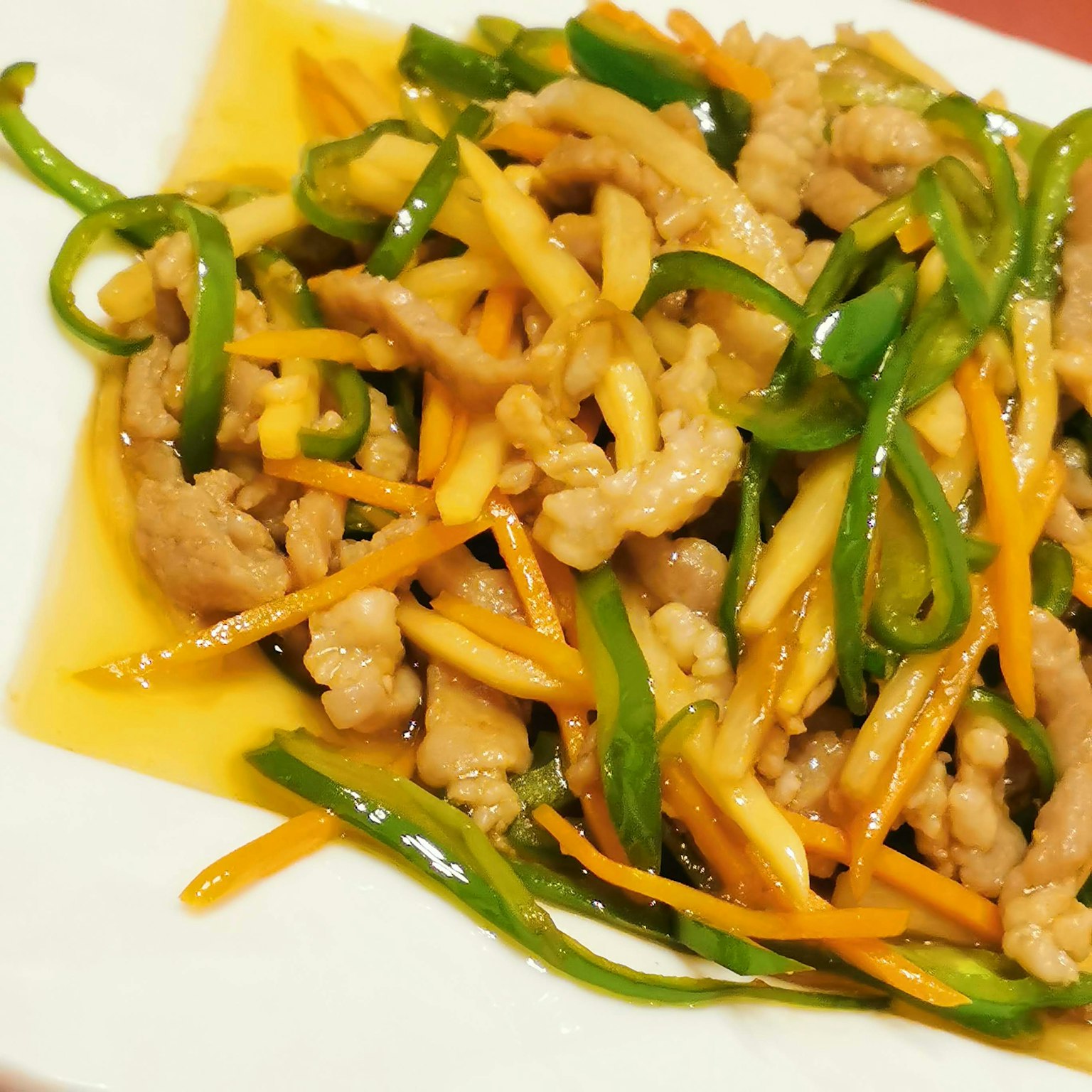 Stir-fried pork with green peppers and carrots served on a white plate