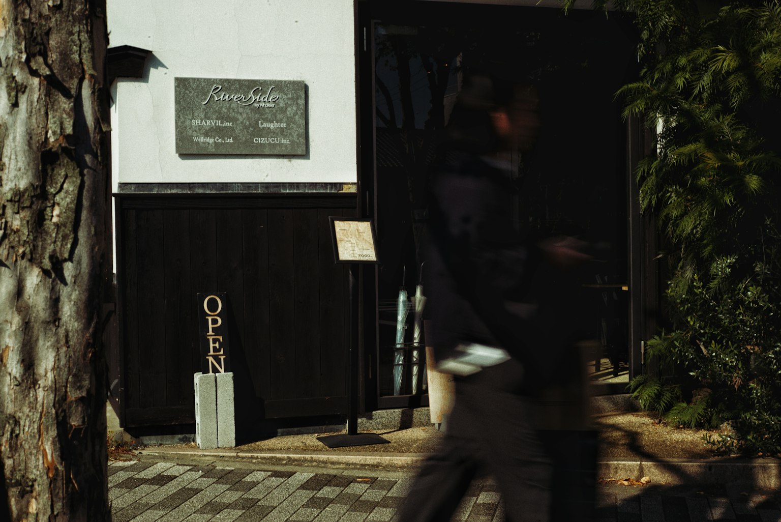 Personas caminando frente a un café con exterior negro y un letrero de ABIERTO