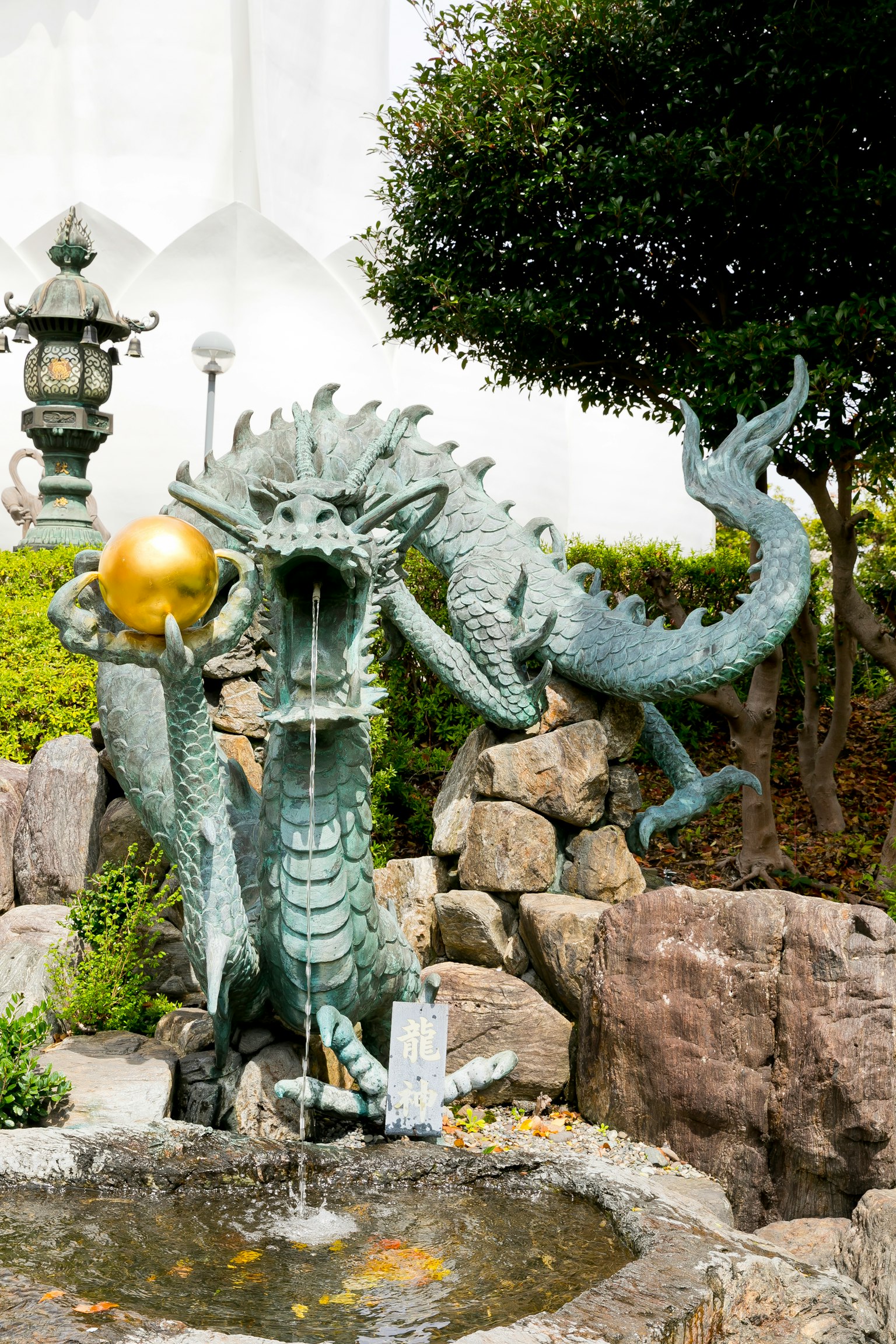 Bronzene Drachenbrunnen, der eine goldene Kugel hält und Wasser fließt