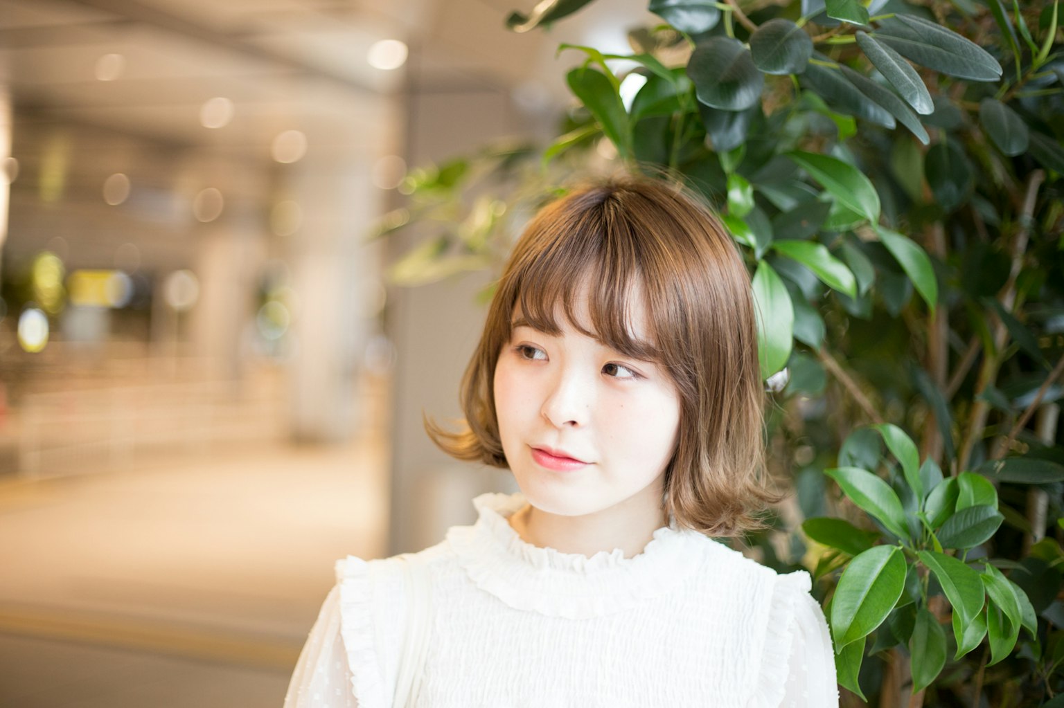 年轻女性穿着白色裙子在绿色植物前微笑