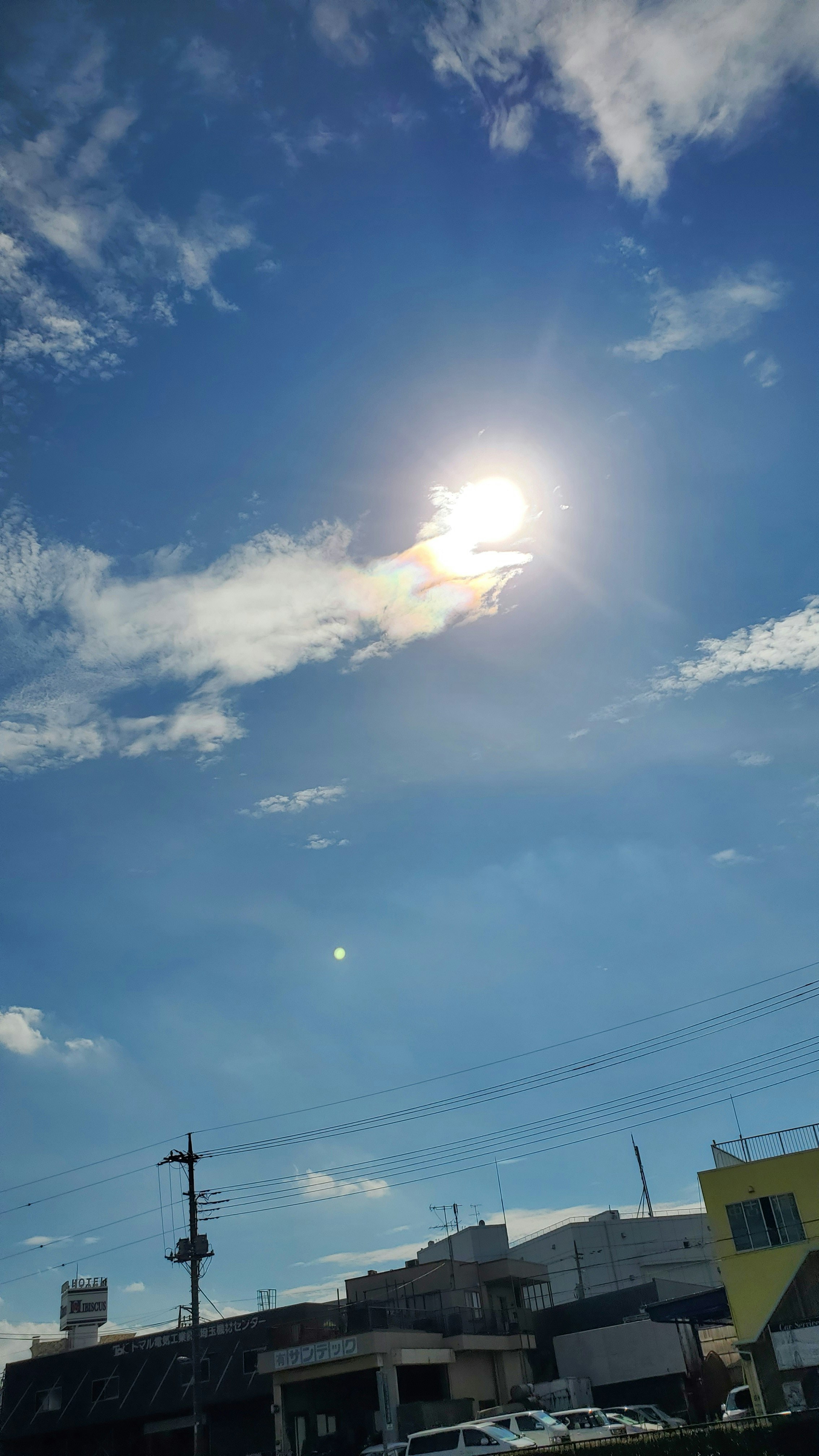 青空に浮かぶ雲と夕暮れの太陽が差し込む街並み