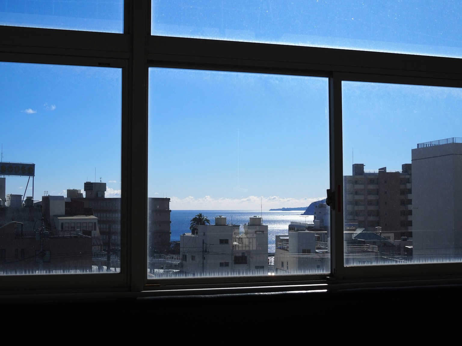 Vue du ciel bleu et de la mer à travers une fenêtre avec des bâtiments urbains