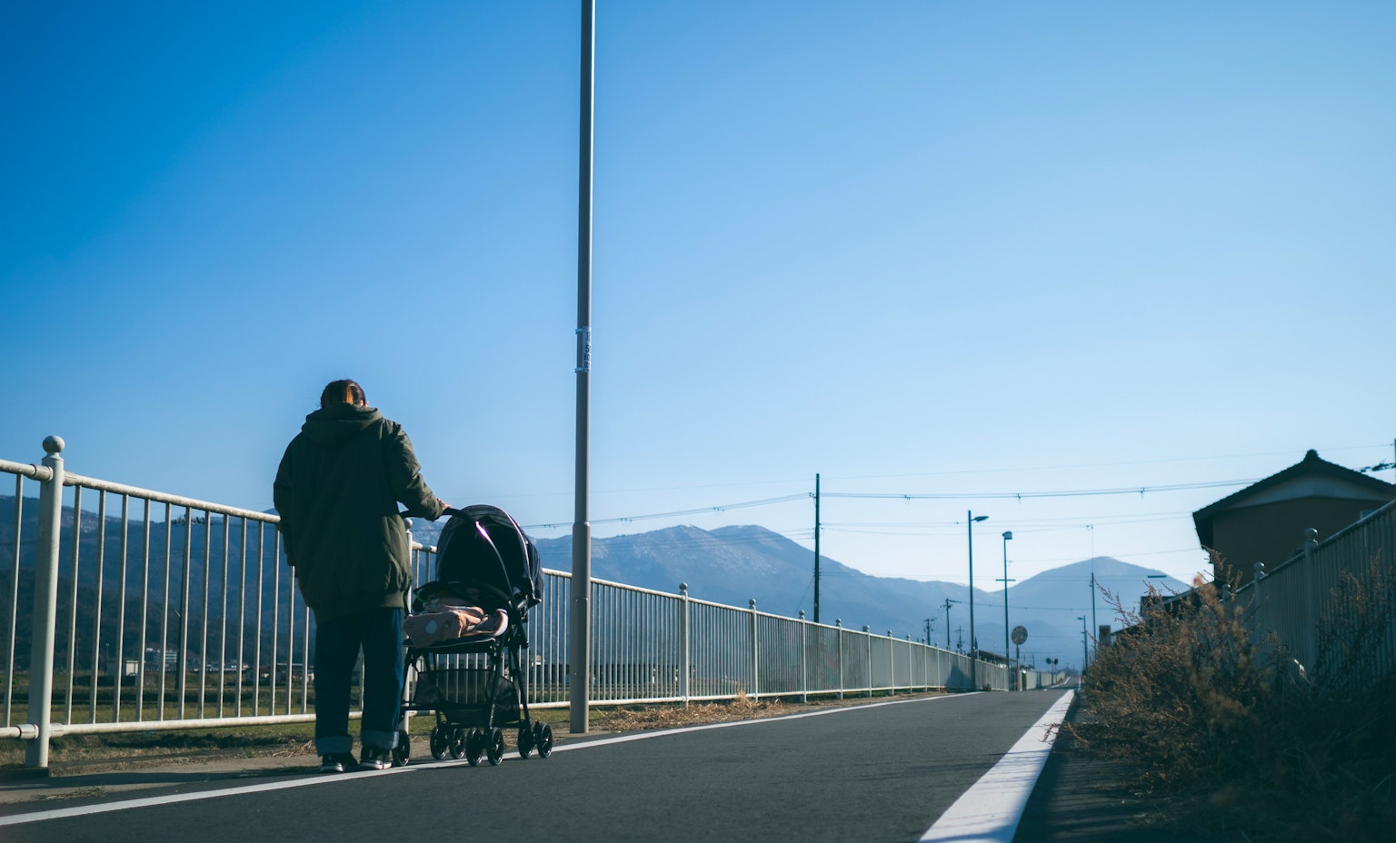 Father pushing a stroller under a blue sky with mountains in the background